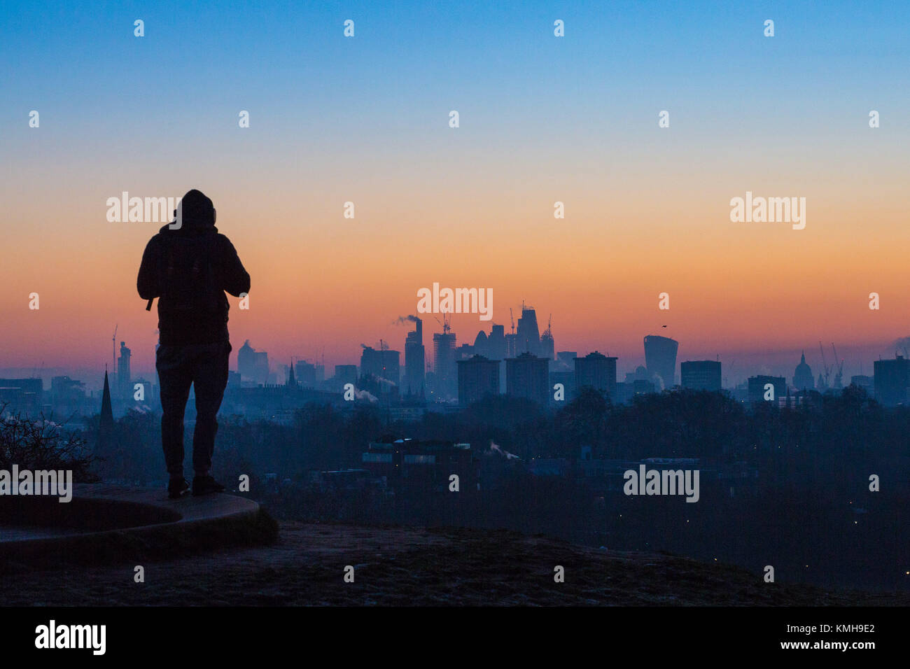 London, UK. 12th Dec, 2017. London, December 12 2017. An early morning walker awaits the sunrise on a clear very cold morning in London, seen from Primrose Hill in Camden. Credit: Paul Davey/Alamy Live News Stock Photo