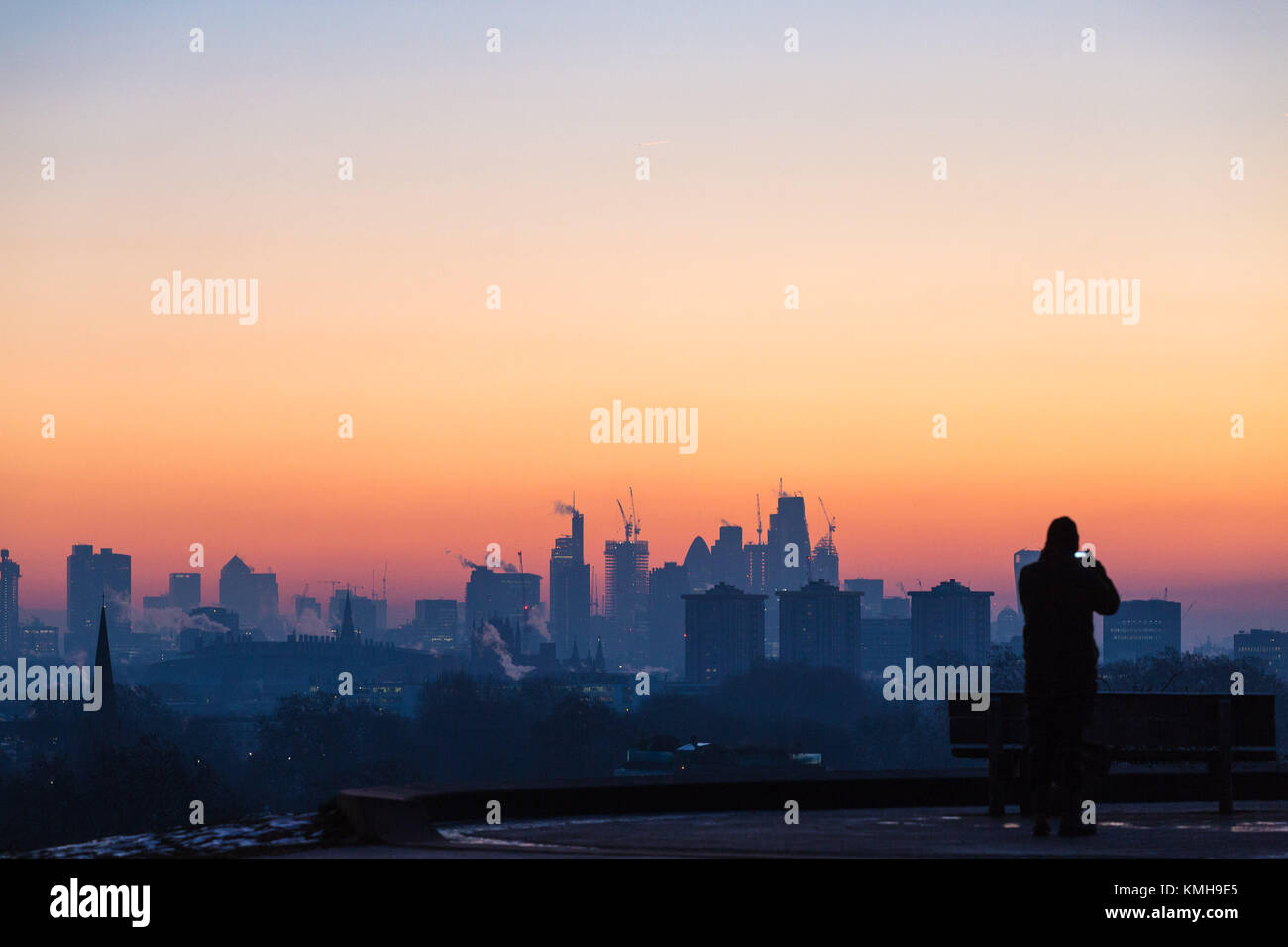 London, UK. 12th Dec, 2017. London, December 12 2017. A walker photographs the skyline before the sun rises on a clear very cold morning in London, seen from Primrose Hill in Camden. Credit: Paul Davey/Alamy Live News Stock Photo