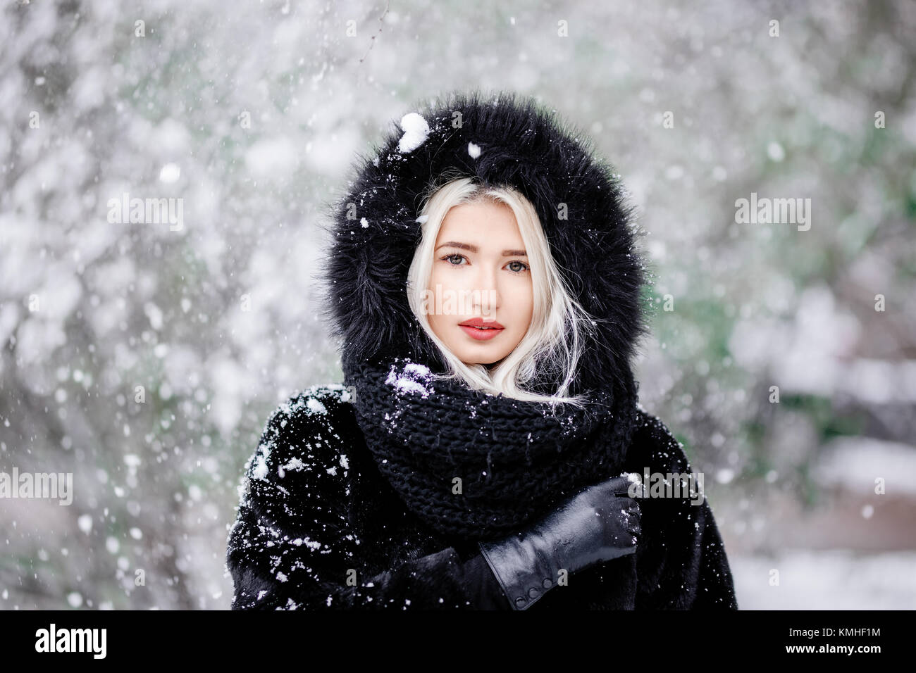 Portrait of beautiful blonde girl in a warm fur coat outdoor in a snowy forest. Stock Photo