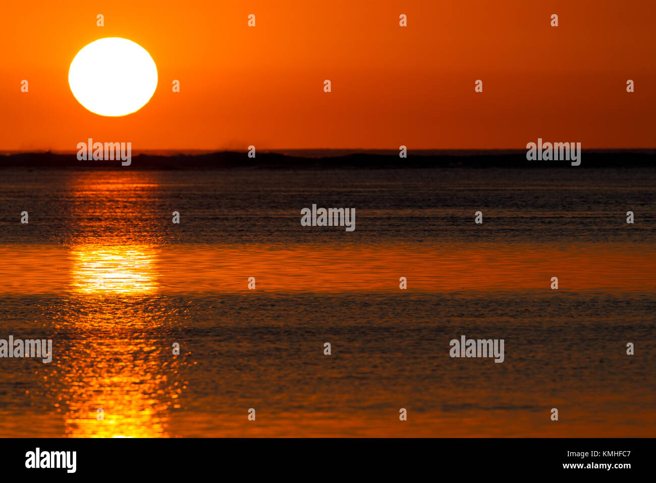 The golden light of the setting sun reflecting in the calm water of the ...