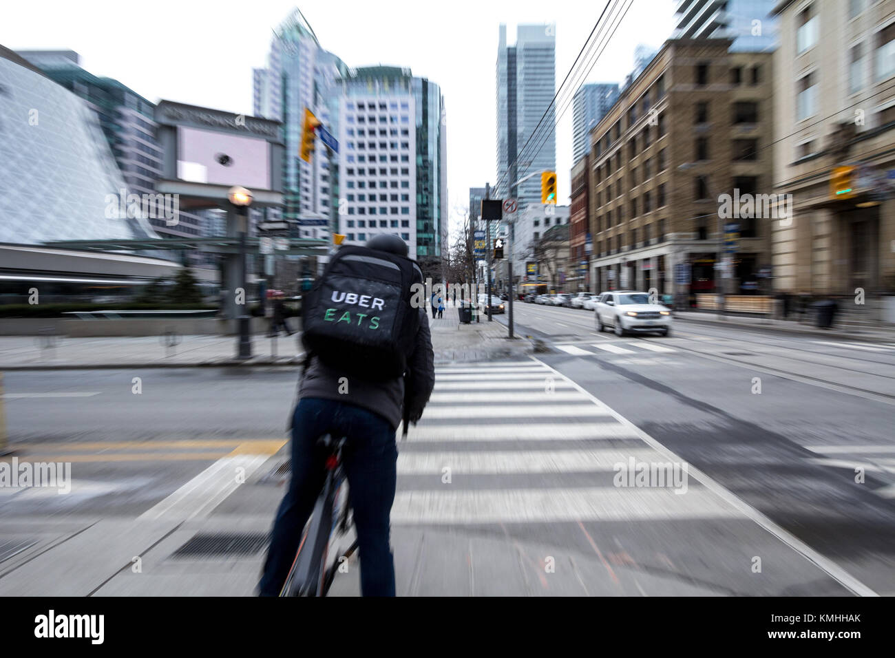 TORONTO, CANADA - DECEMBER 31, 2016: Uber Eats delivery man on a bicycle waiting to cross a street in the center of Toronto, Ontario, with a motion bl Stock Photo