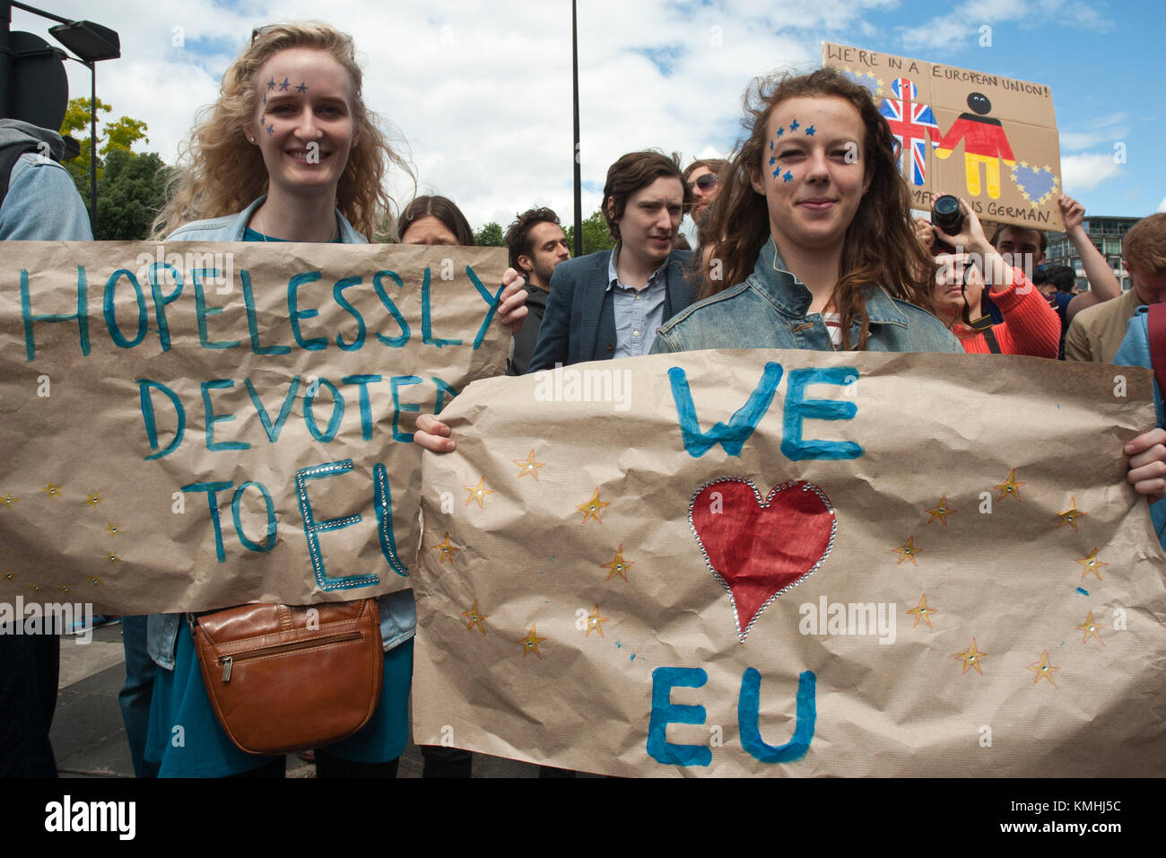 Two young women with blue/gold stars on face, with banners 'We love EU', 'Hopelessly devoted to EU'. Colourful, youthful. Stock Photo