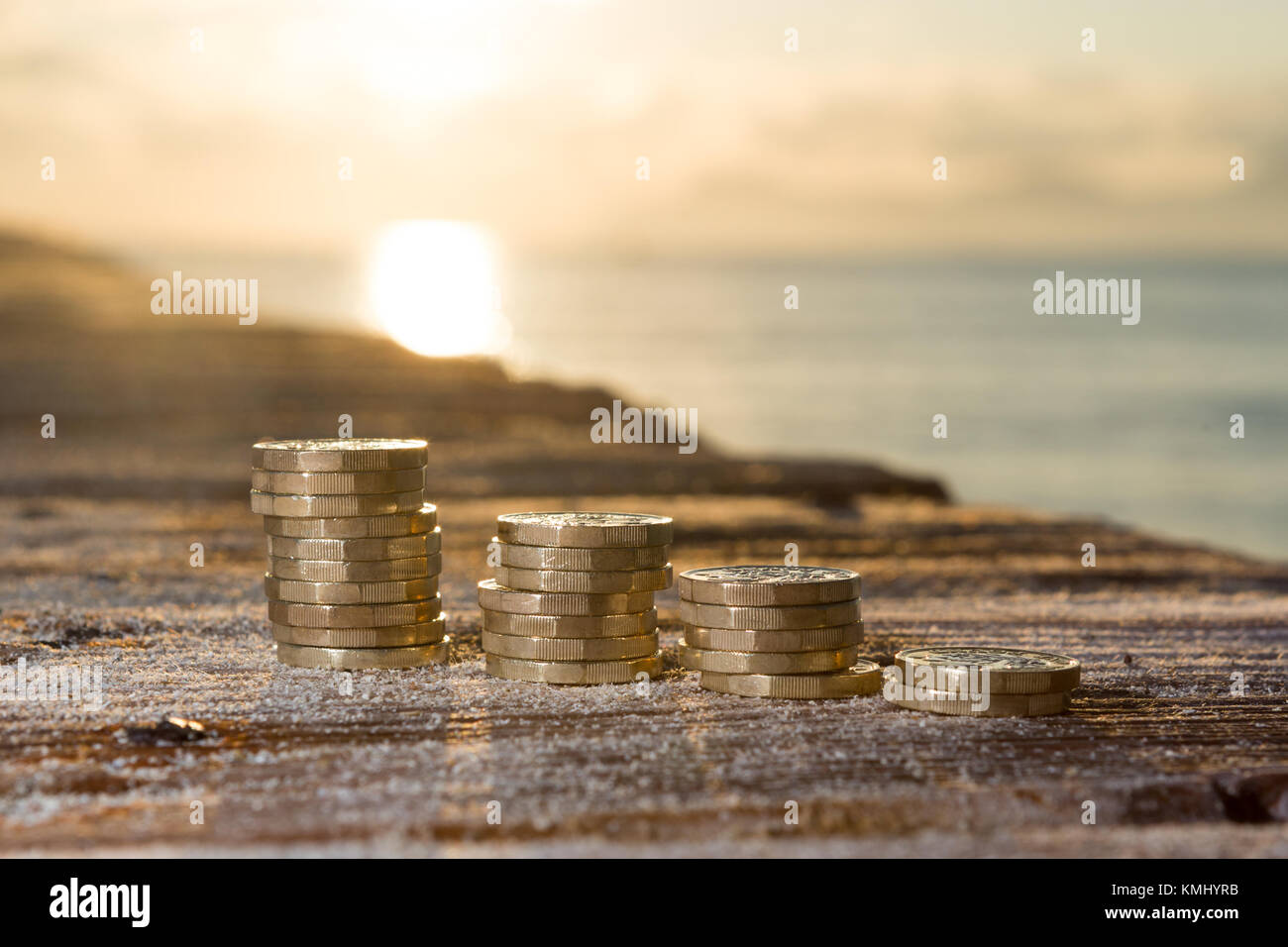 British Money, Pound Coins in Rising Stacks on Sandy Wood. New Pounds in a Warm Sunrise Light. Stock Photo