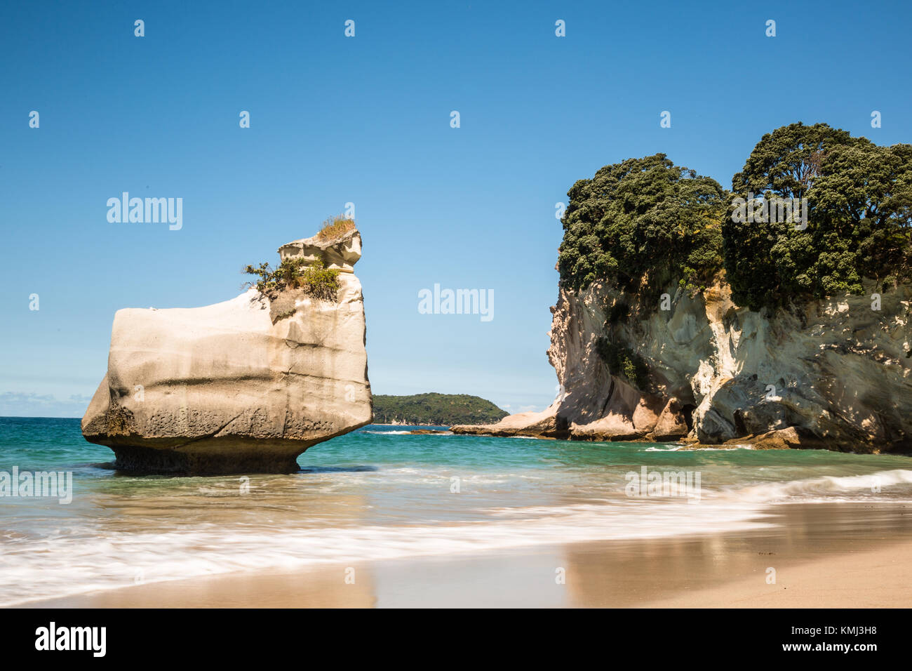 A sea stack, a section of rock formerly attached to the main land formation and separated by erosion, stands above a sandy beach in the Coromandel reg Stock Photo