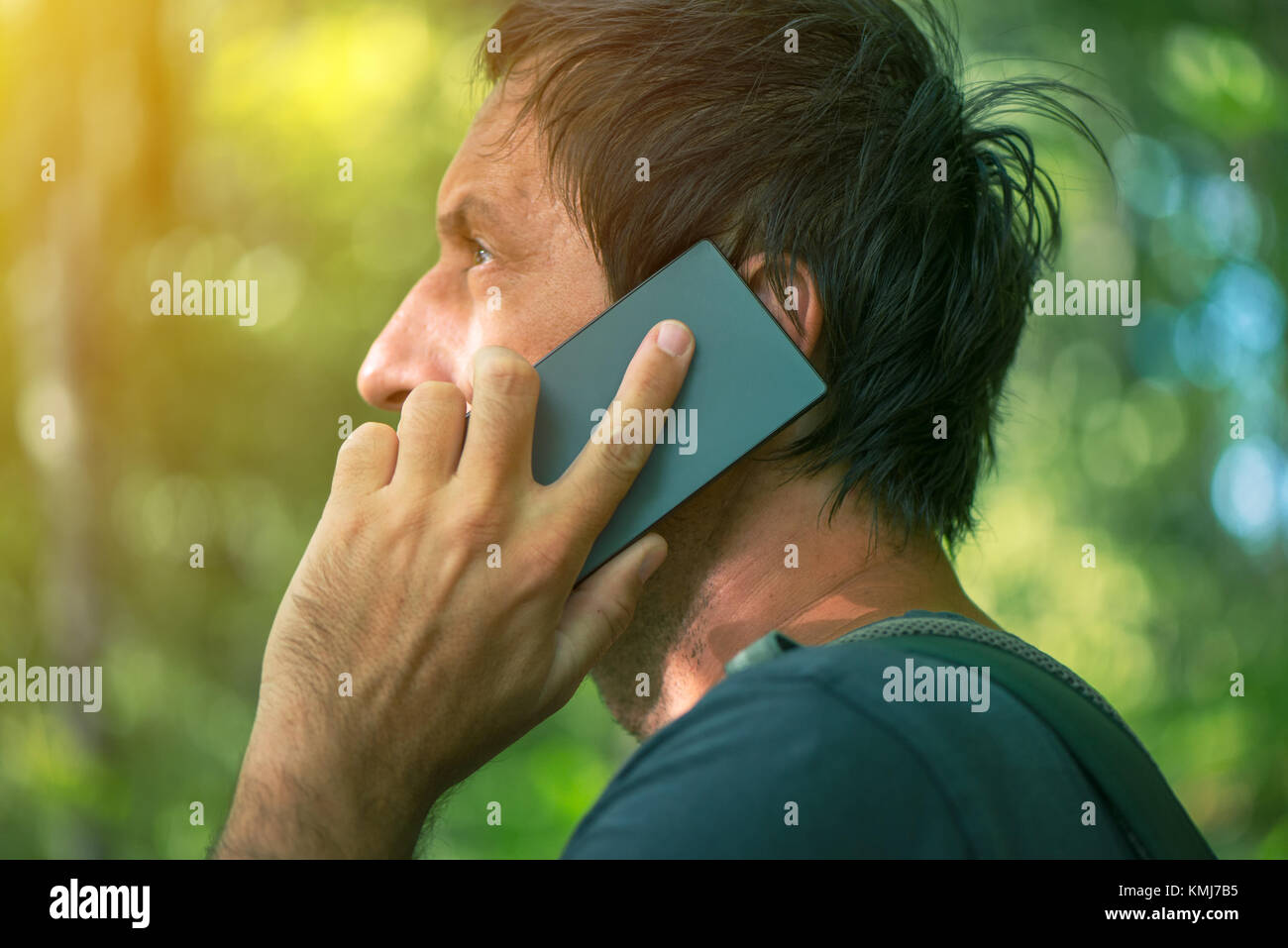 Man talking on mobile phone in park, adult male backpacker walking outdoors and using smartphone for communication. Stock Photo