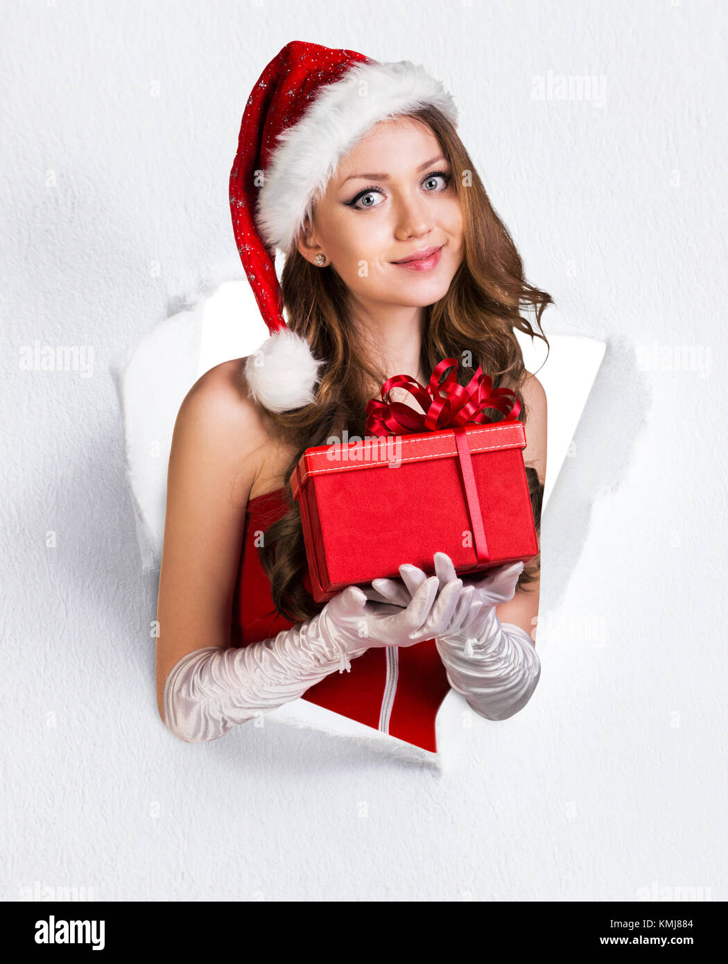 Woman in santa's costume with gift tears up from paper hole. Stock Photo