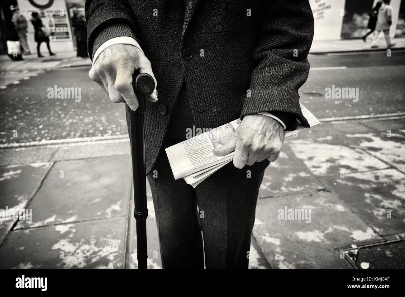 Primer plano de un hombre mayor irreconocible con un baston en una mano y un periodico en la otra. Oxford St., Londres, Uk, Europa. Stock Photo