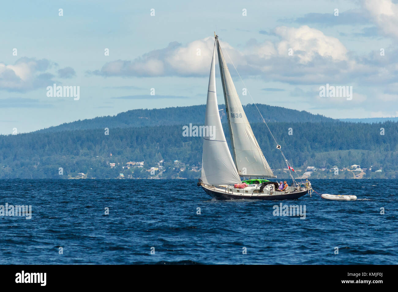 On a summer day, a middle-aged couple are at the helm of a Canadian yacht under sail in Malaspina Strait, near Powell River, British Columbia. Stock Photo