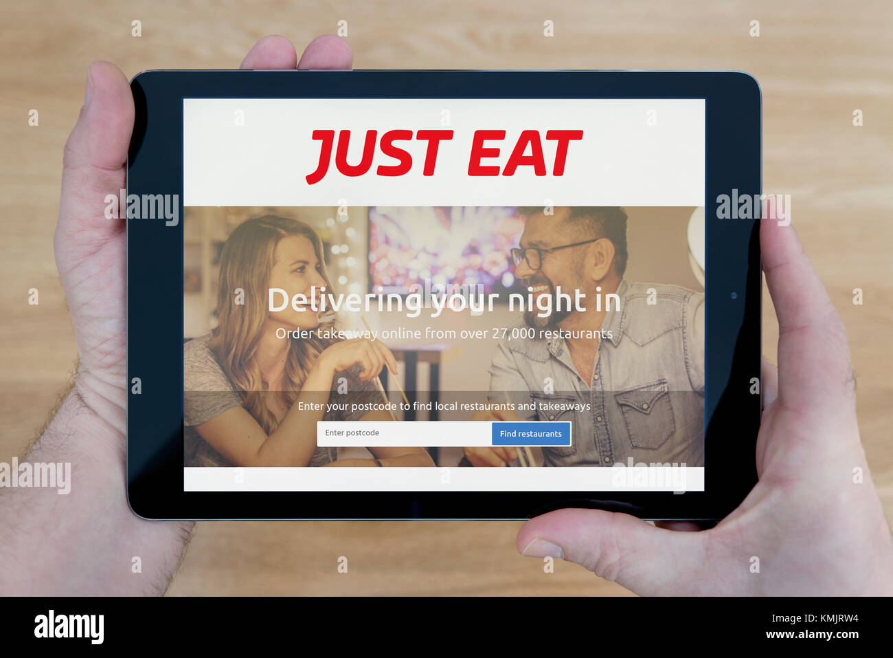 A man looks at the Just Eat website on his iPad tablet device, shot against a wooden table top background (Editorial use only) Stock Photo