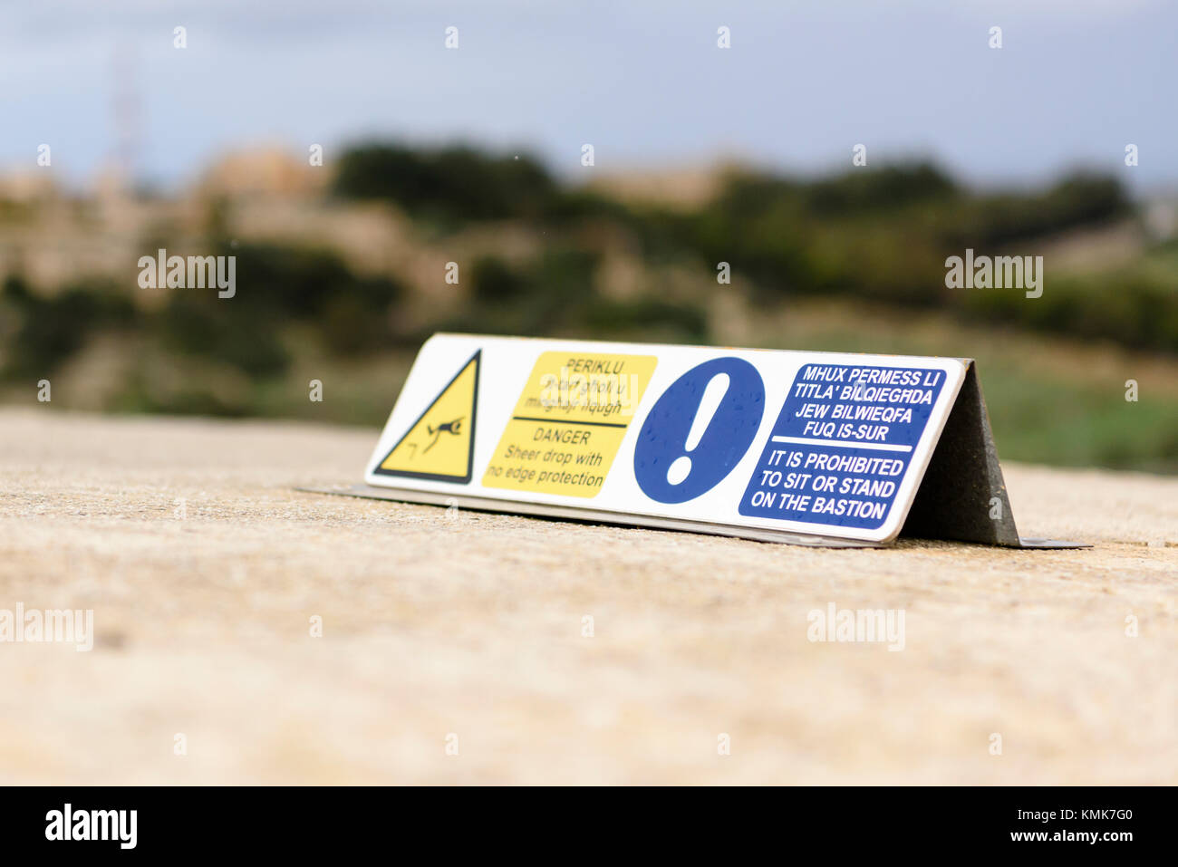 Sign warning visitors not to sit or stand on the bastion ramparts of Mdina Walled City, due to the sheer drop on the other side. Stock Photo