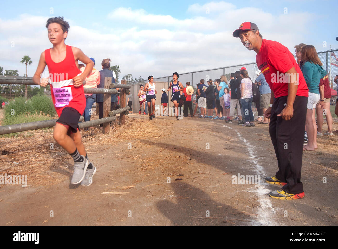 A high school track coach cheers on a teenage boy running a cross country foot race at a high