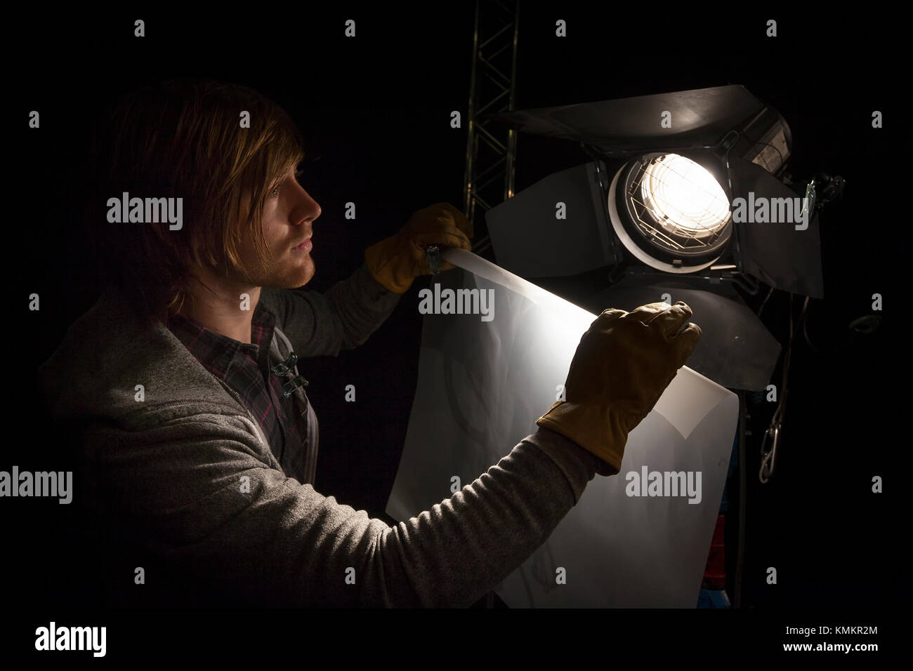 Lighting man placing a sheet of diffuser on a studio light in a Television studio Stock Photo