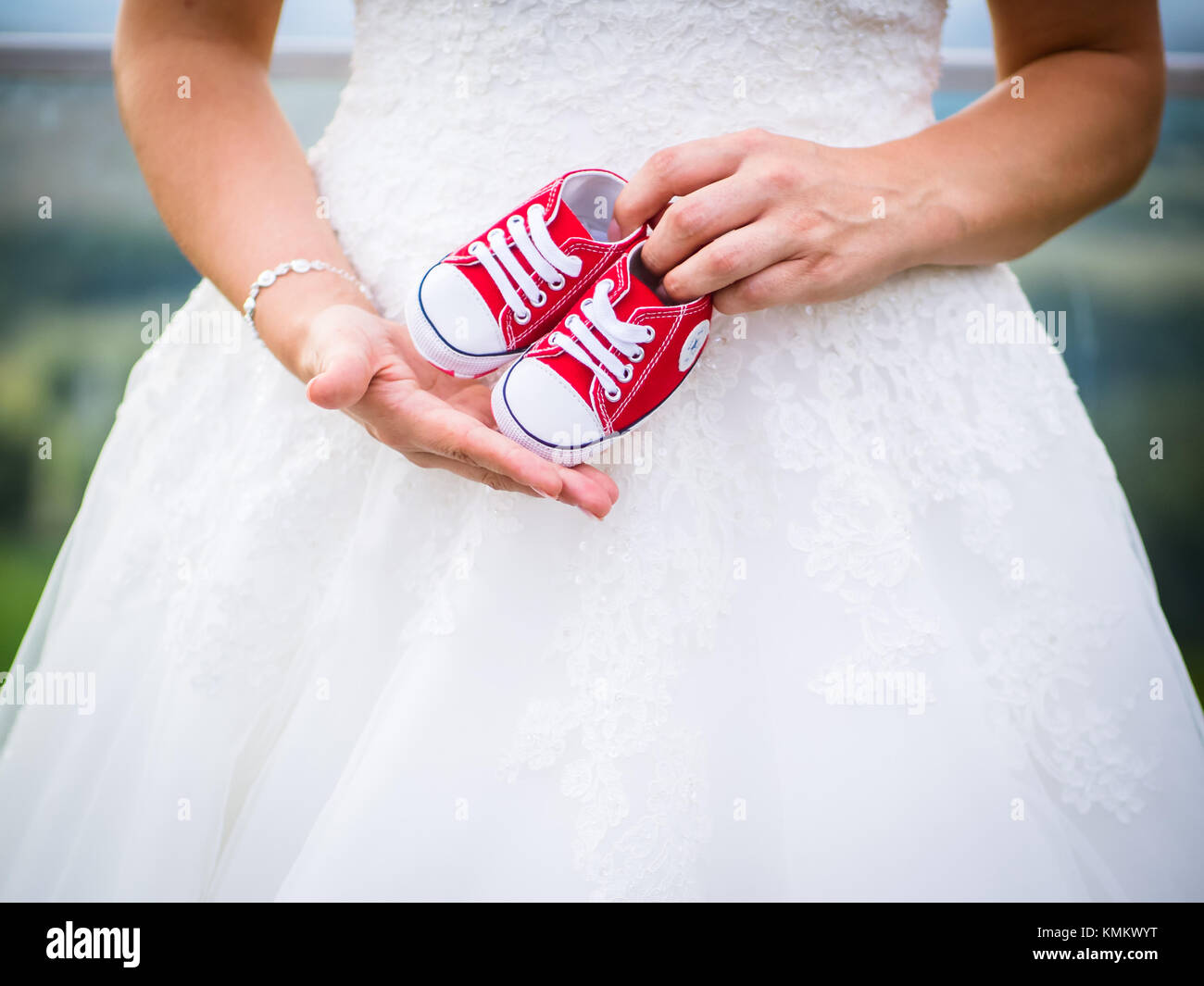 The pregnant bride has the little baby shoes in front of her stomach Stock Photo