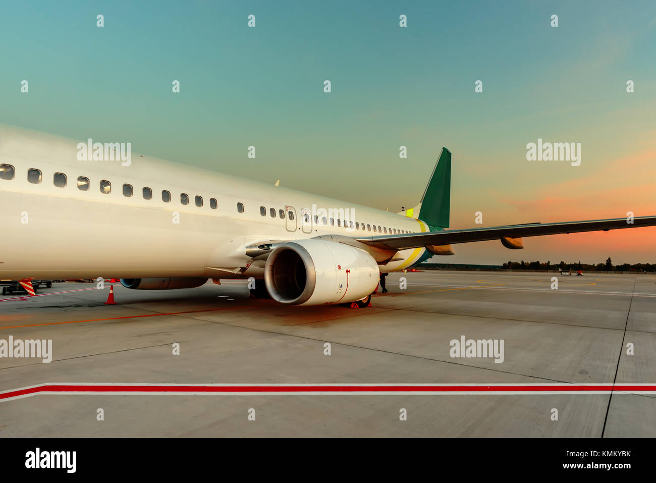 A white plane with a turbine stands on concrete slabs of an airfield in the light of the evening dawn Stock Photo