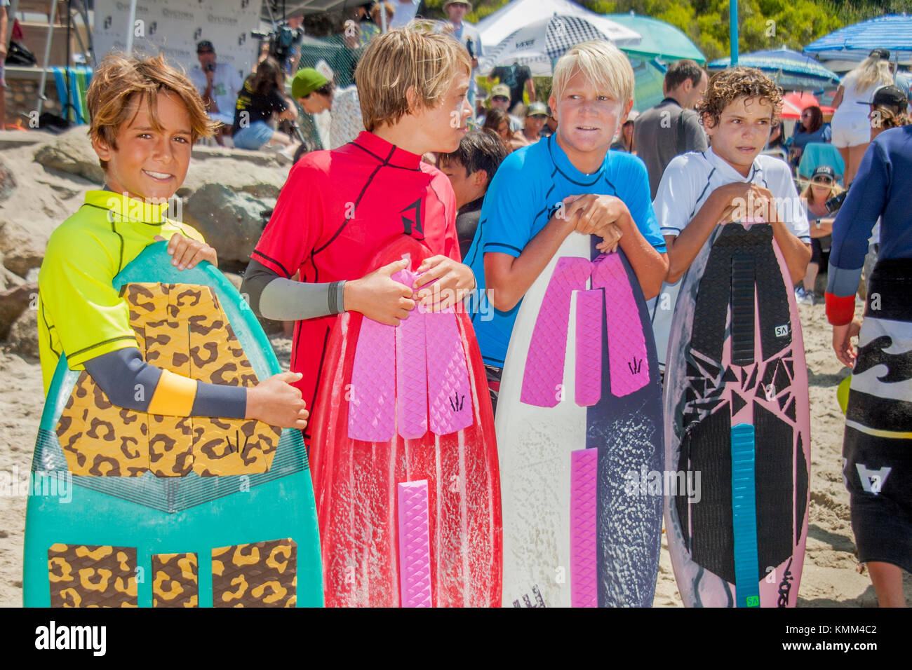 Four teen boys in wetsuits pose with their skimboards in Laguna Beach, CA. Surf riders typically