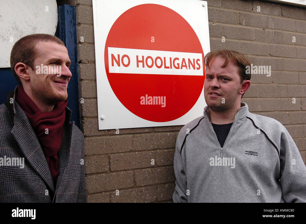 Sports journalist chatting next to 'No Hooligans' sign banning hooligans from Cardiff City Football Club Stock Photo