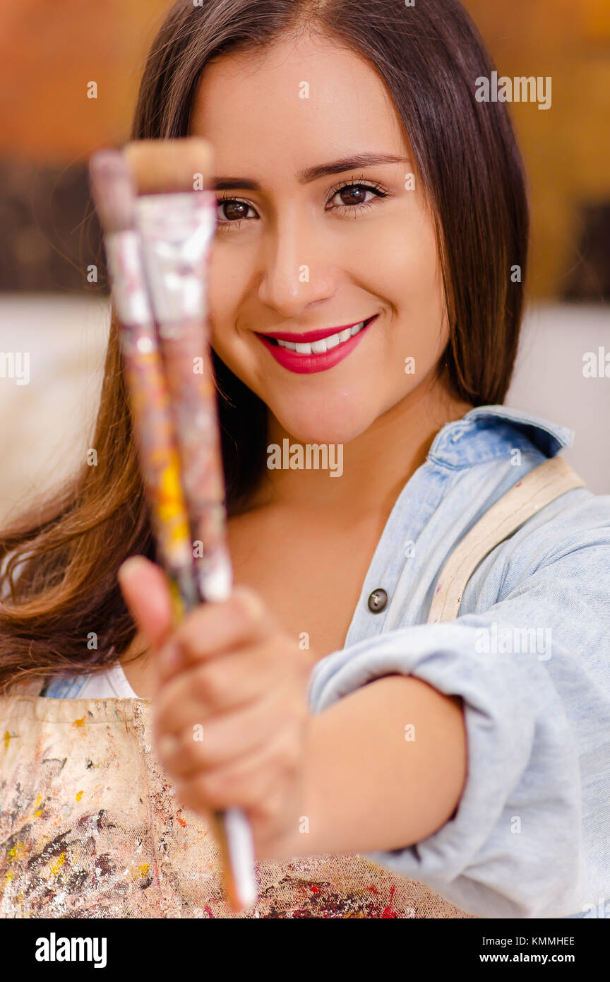 Beautiful young woman painter with paint brush in hands, in a blurred