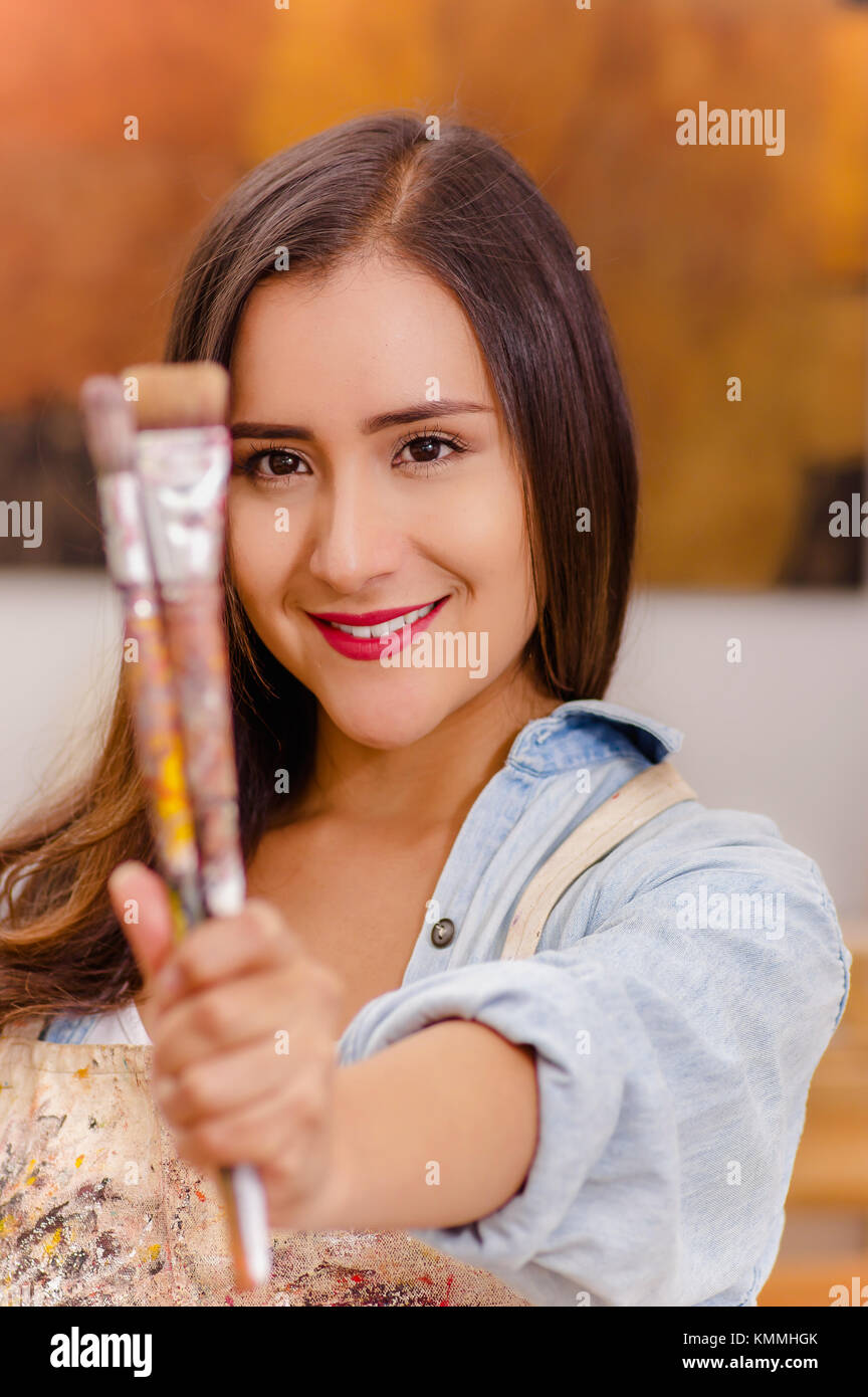 Beautiful young woman painter with paint brush in hands, in a blurred