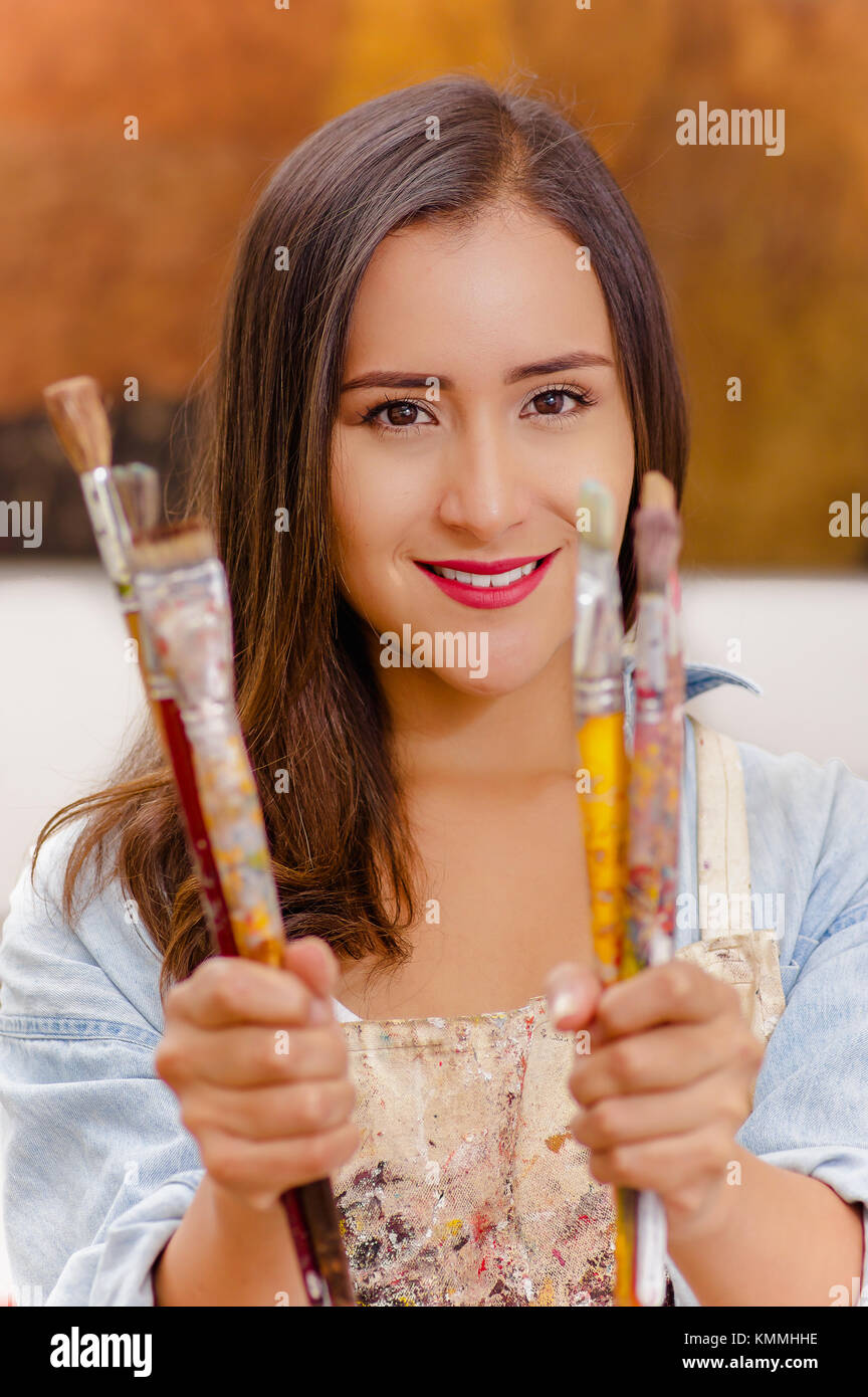 Beautiful young woman painter with paint brush in hands, in a blurred