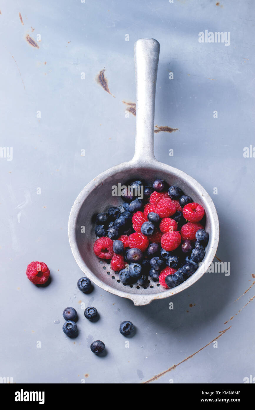 Aluminium colander with fresh raspberries and blueberries over gray ...