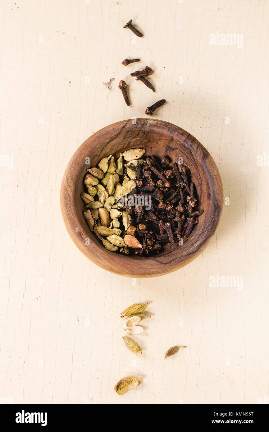 Cardamom seeds and cloves in olive wood bowl over white wooden