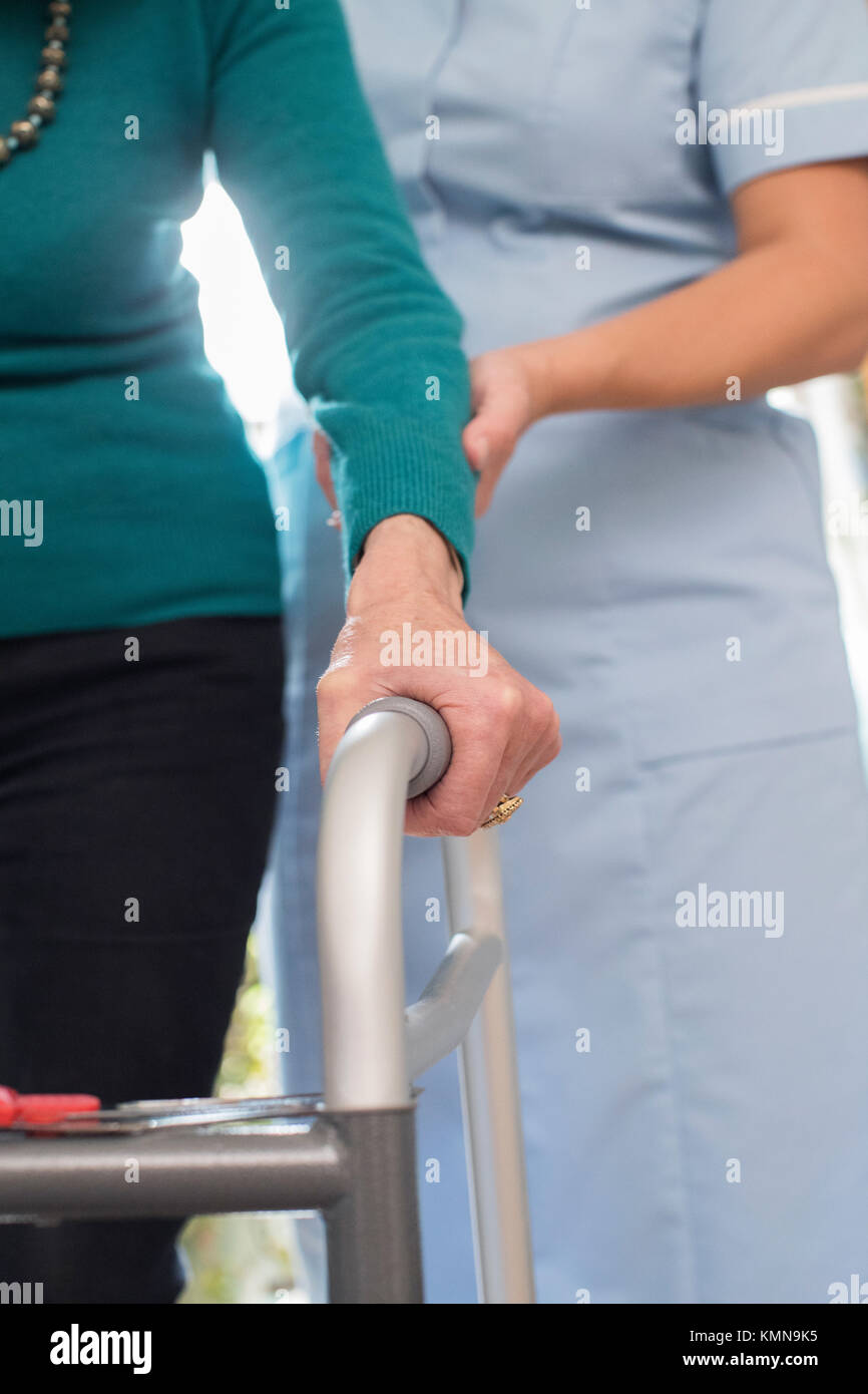 Senior Woman's Hands On Walking Frame With Care Worker In Background Stock Photo