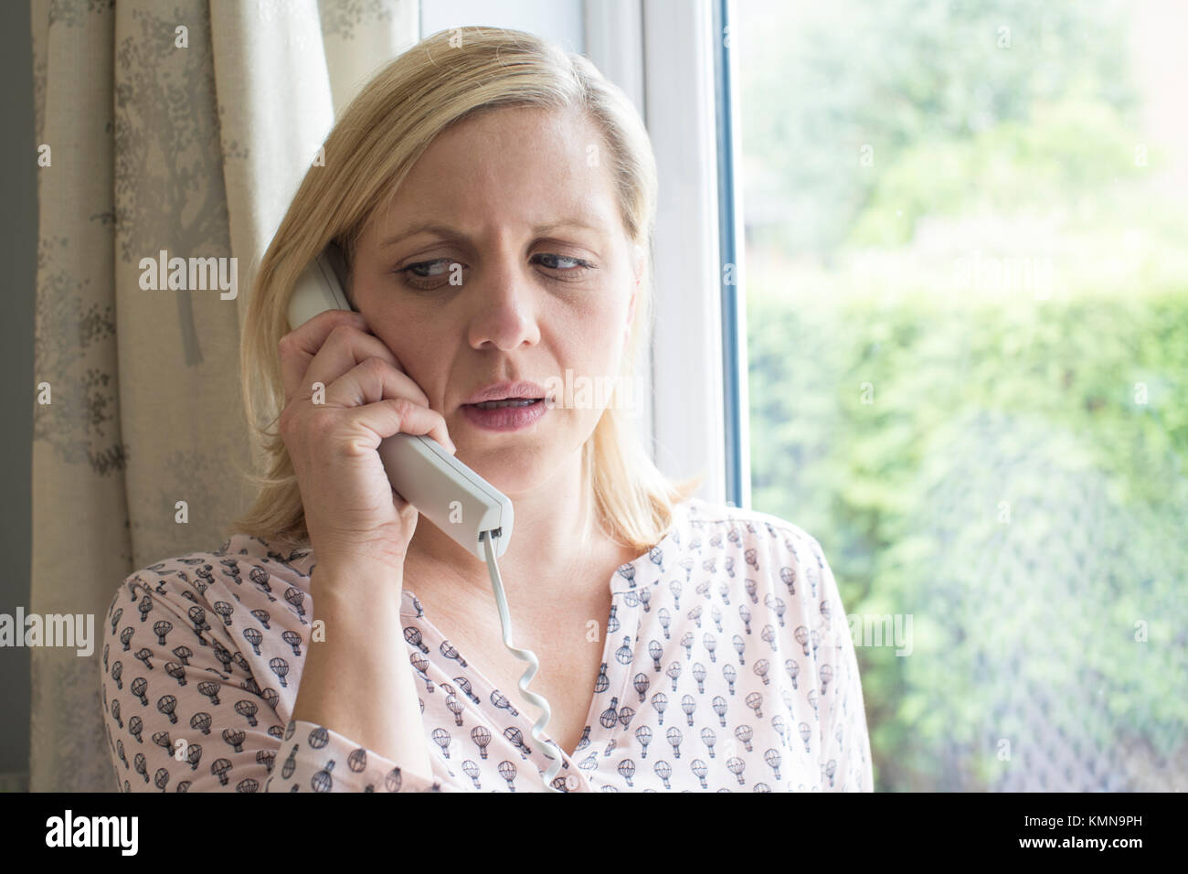 Worried Woman Answering Telephone At Home Stock Photo