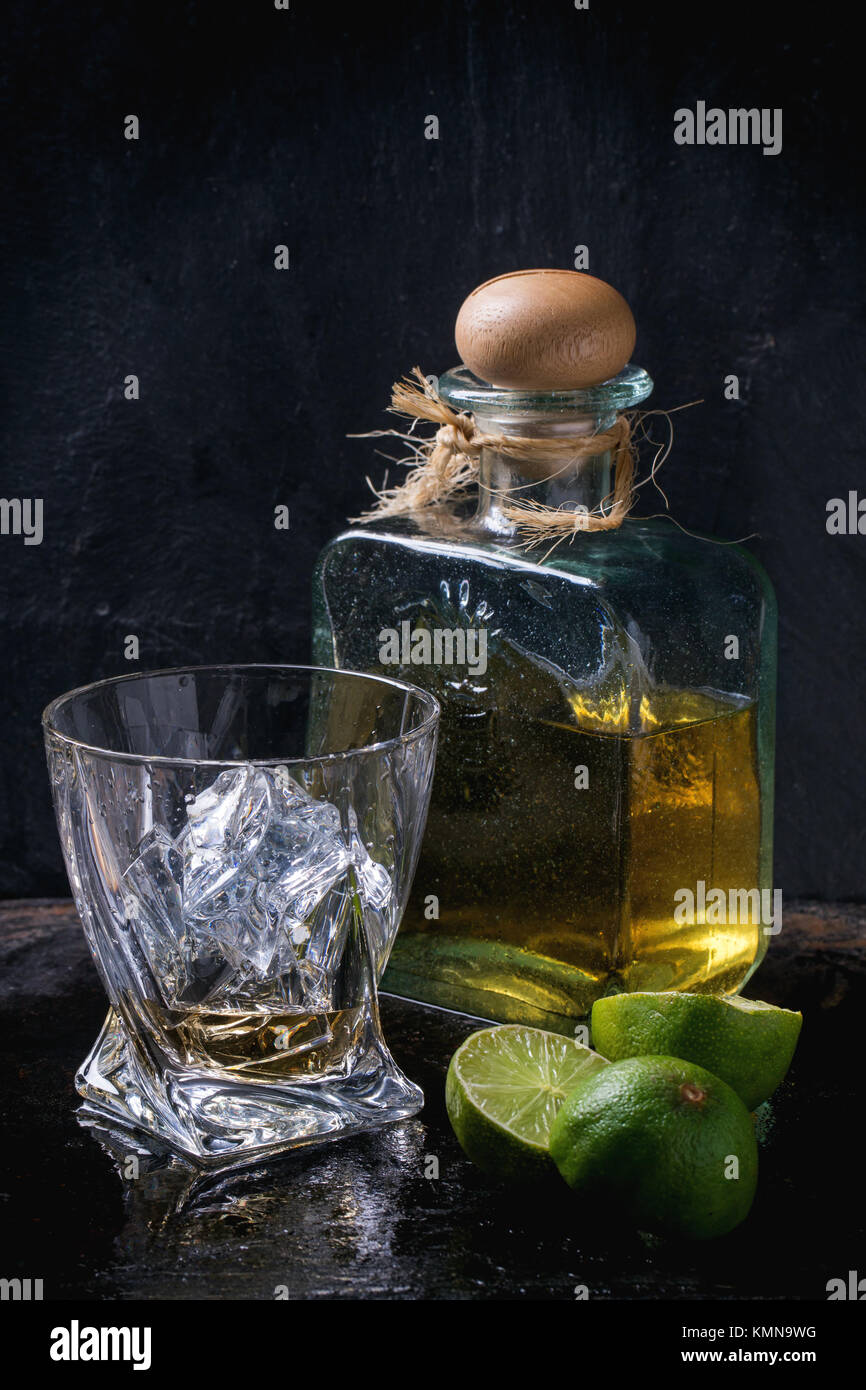 Glass of anejo tequila with ice cubes and bottle of tequila, served