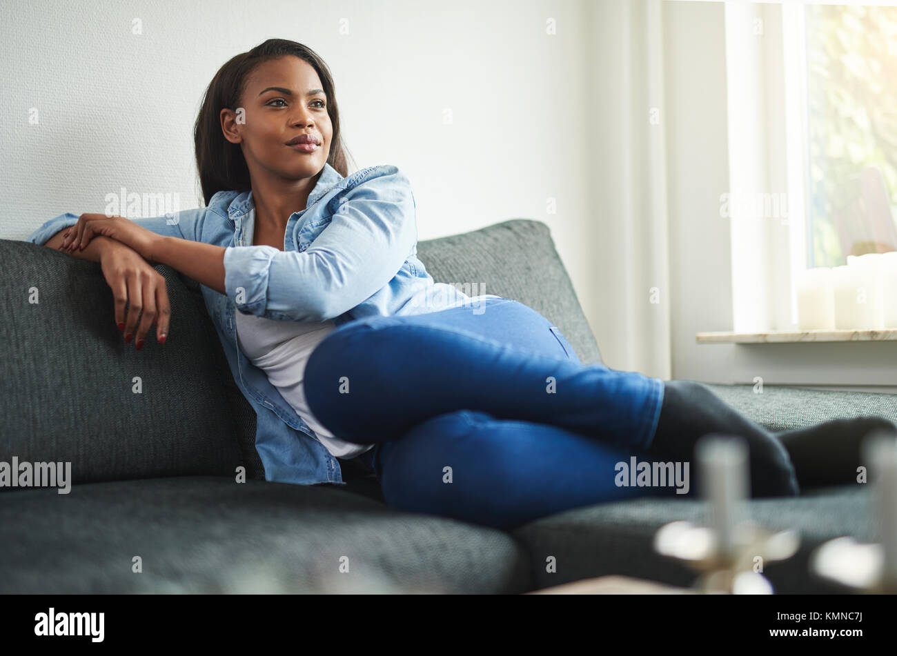 Casually dressed young African woman smiling while relaxing at home on ...