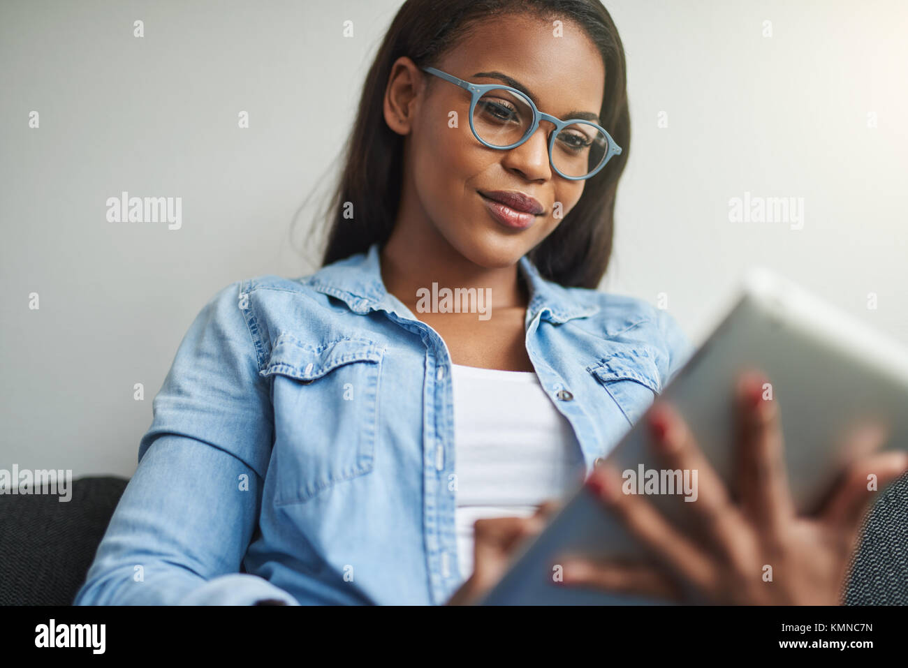 Smiling young African woman sitting on her living room sofa using a ...