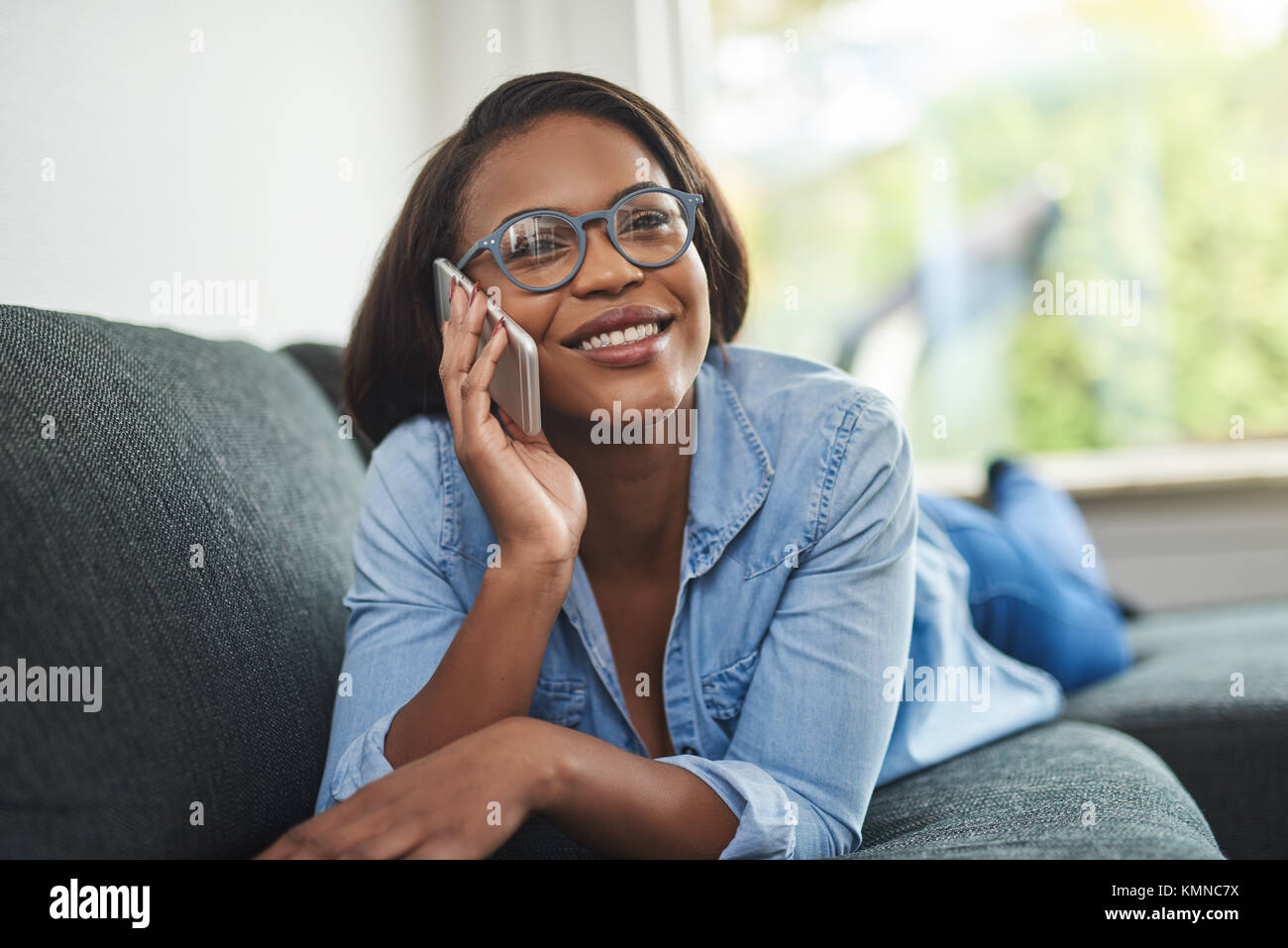 Smiling young African woman wearing glasses lying on her living room ...