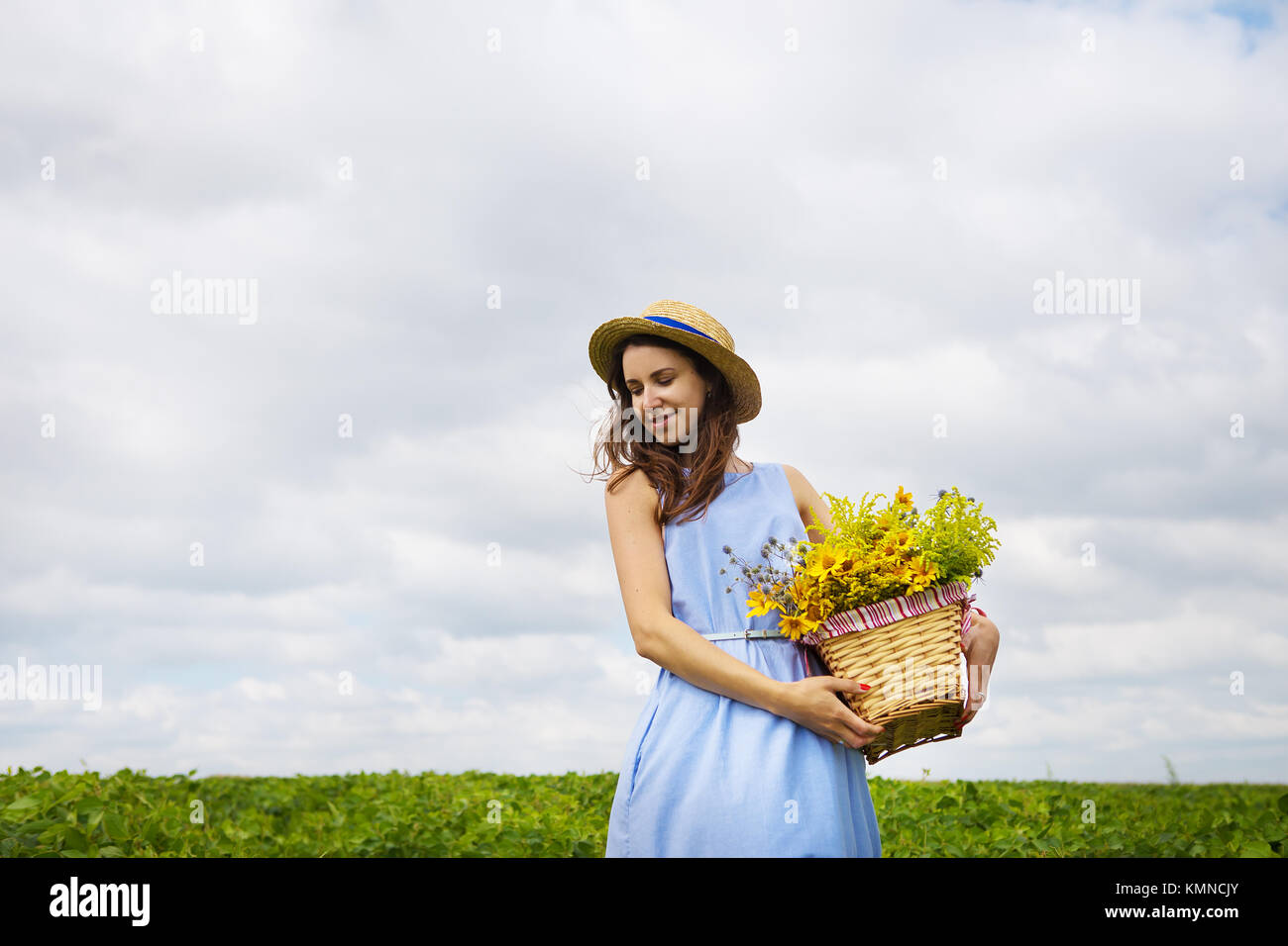 girl in a hat stands on a green field with a basket of flowers Stock ...