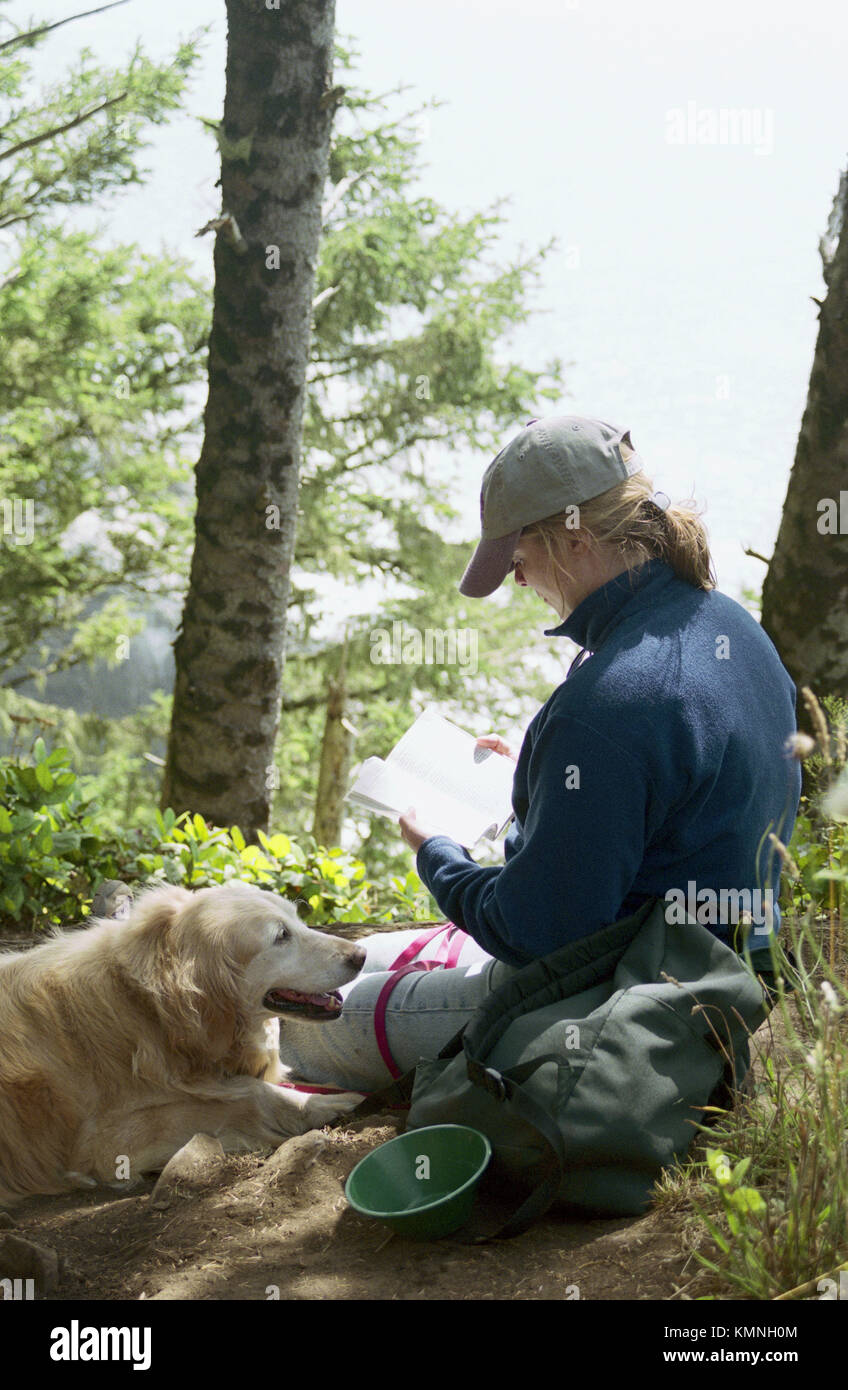 34 year old woman reading book in forest with Golden Retriever. Oregon