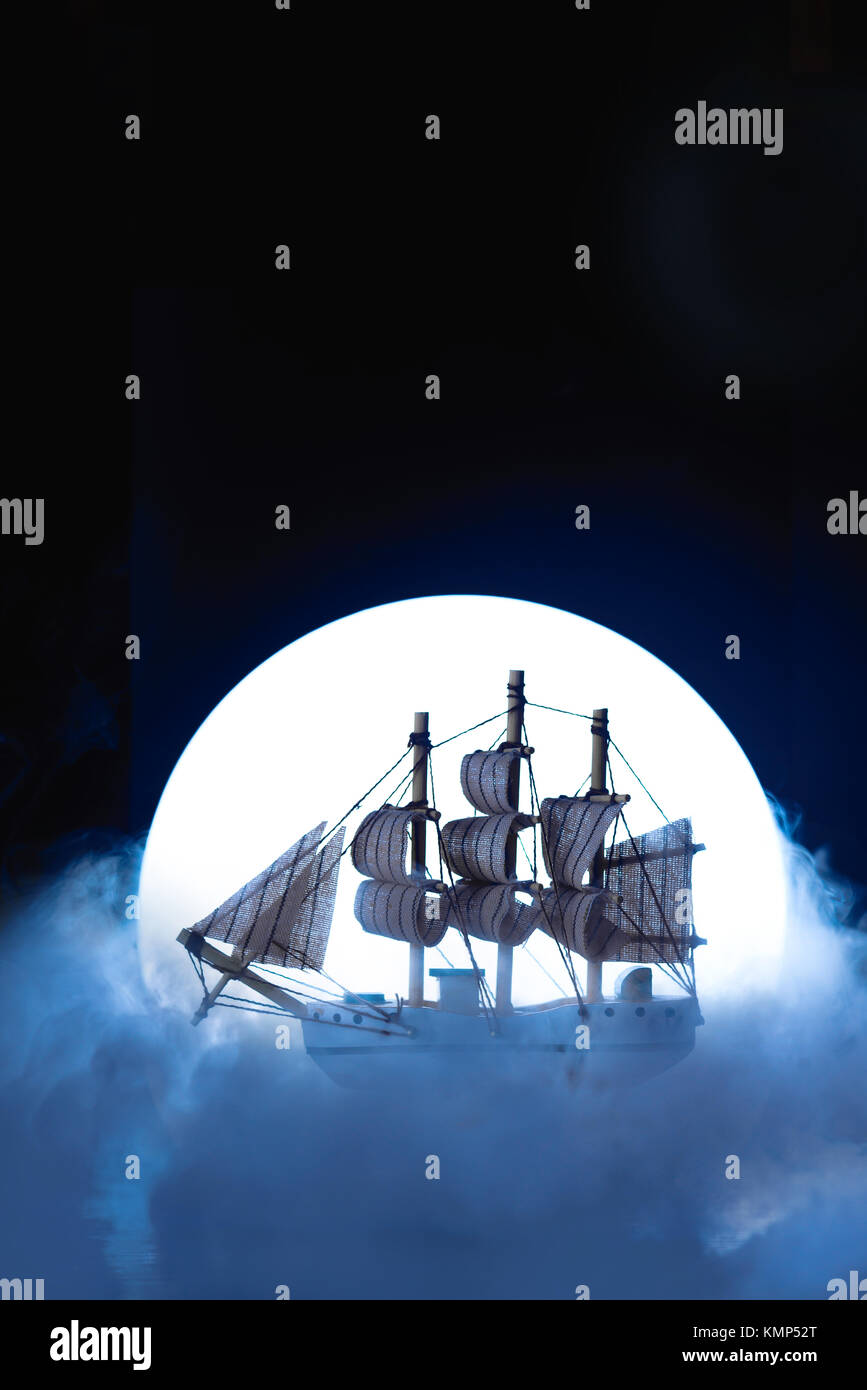 Sail ship in light of full moon. Wooden model on dark background. Conceptual marine still life. Stock Photo