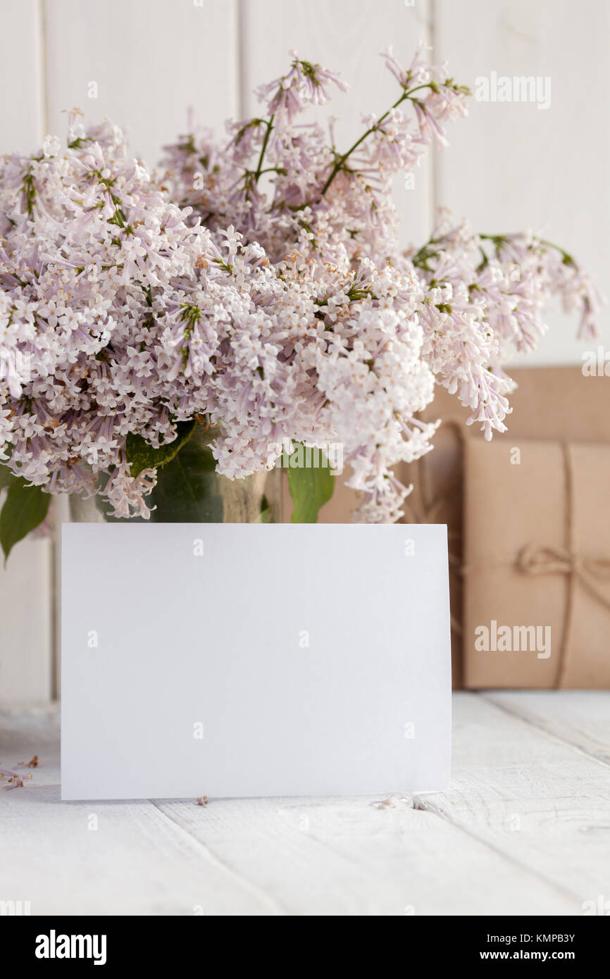 Blank white greeting card with lilac flowers bouquet and envelope on white wooden background. mock up. Stock Photo