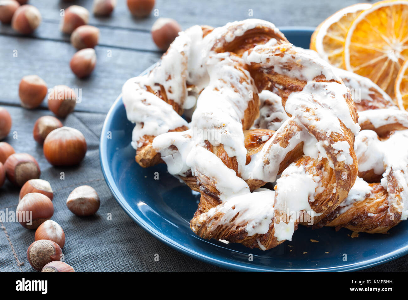 Bavarian cream puff with crushed hazelnut and lemon fondant on a blue plate. In the background a cup of tea and slices of dried oranges. Stock Photo