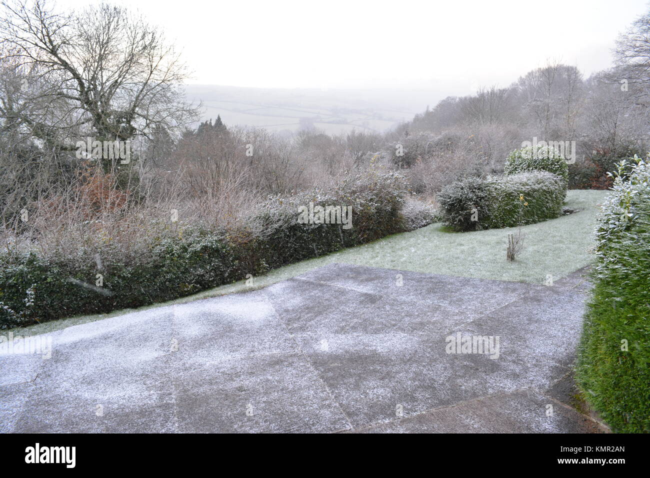 Large sloping garden and concreted driveway in winter with slight snow covering on lawn shrubs trees bushes and beds in south herefordshire england UK Stock Photo