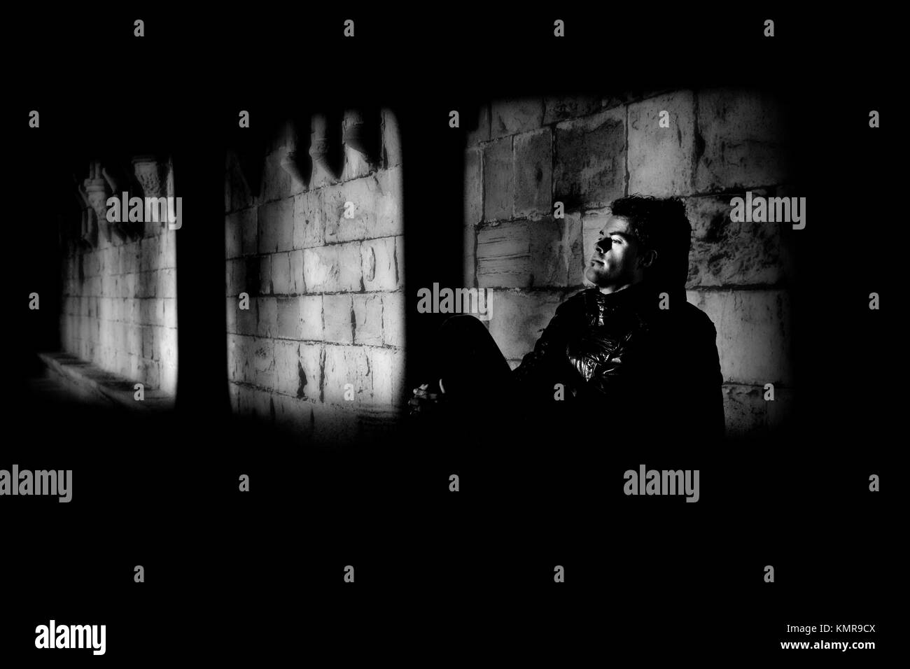 Young man leaning against the wall and meditating in the dark Black and