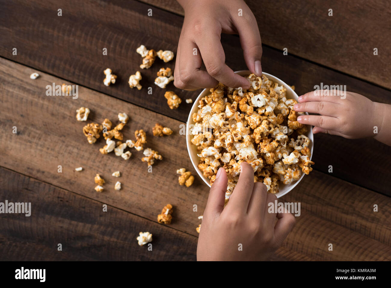 3 kids sharing eating popcorn in a bowl on a wooden table background. sharing concept. Stock Photo