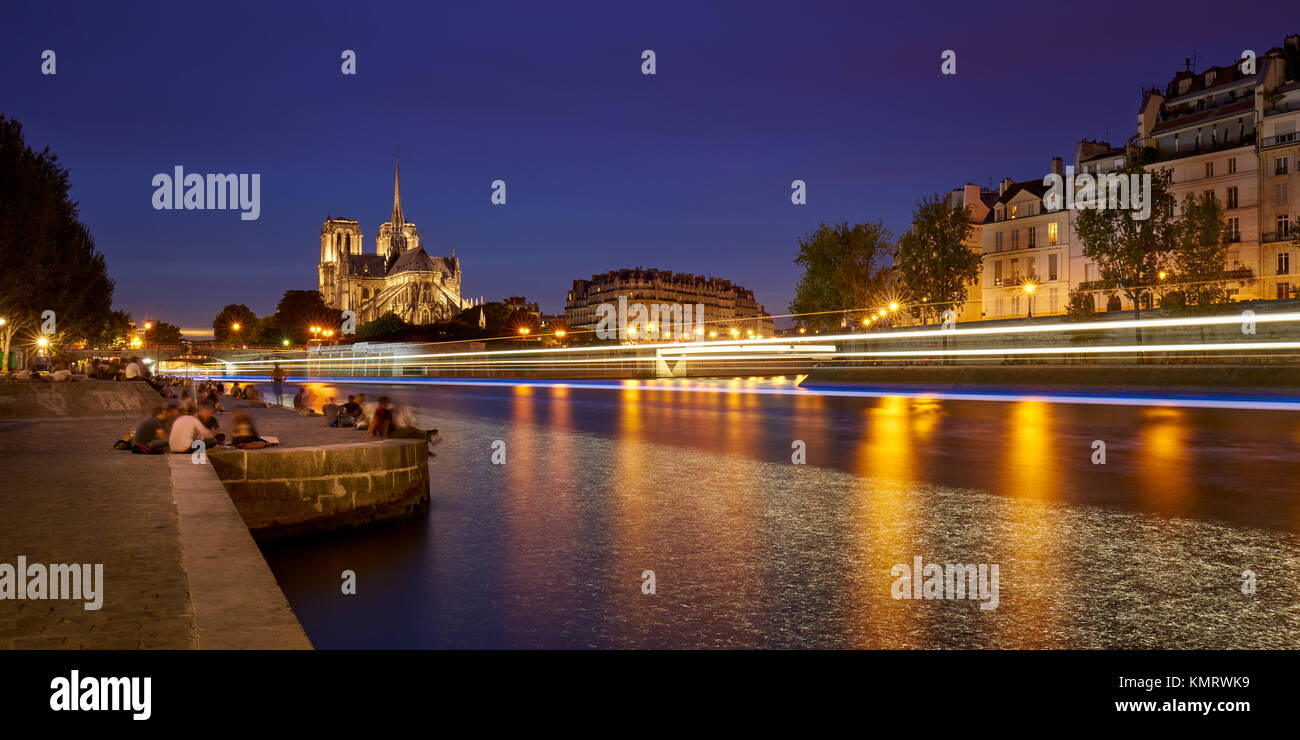 Summer evening on the Seine River banks with Notre Dame de Paris cathedral illuminated. Ile de La Cite and Ile Saint Louis, Paris, France Stock Photo