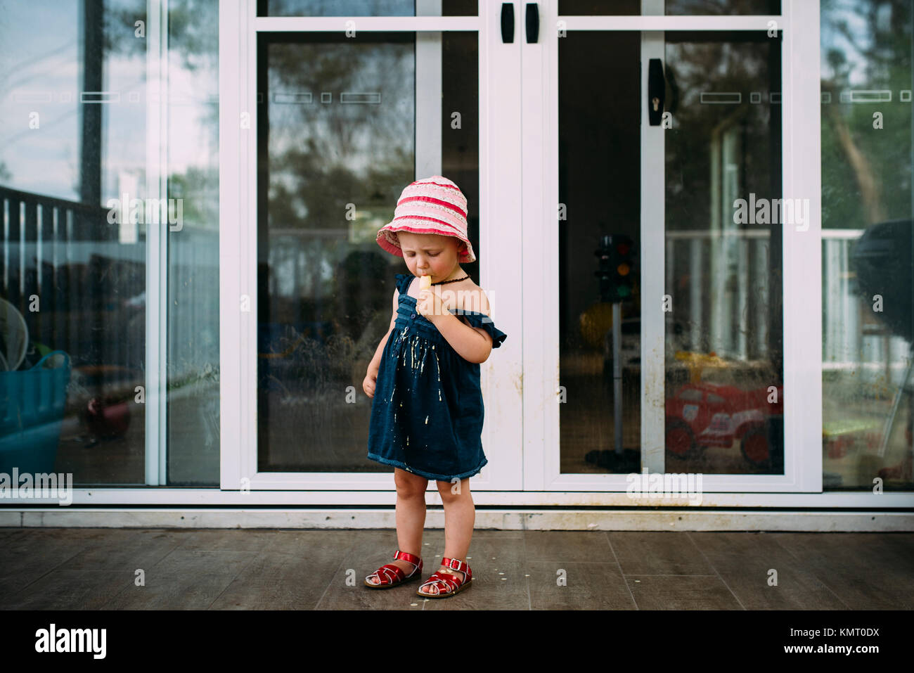 Girl eating flavored ice while standing in porch Stock Photo