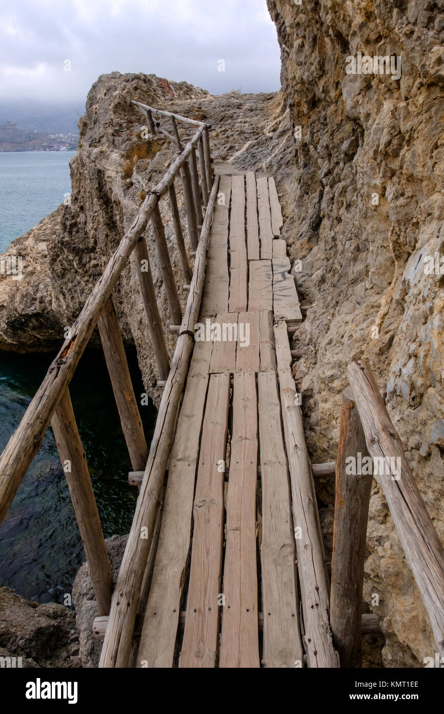 Flimsy old rotten bridge across the rocks on the sea coast Stock Photo