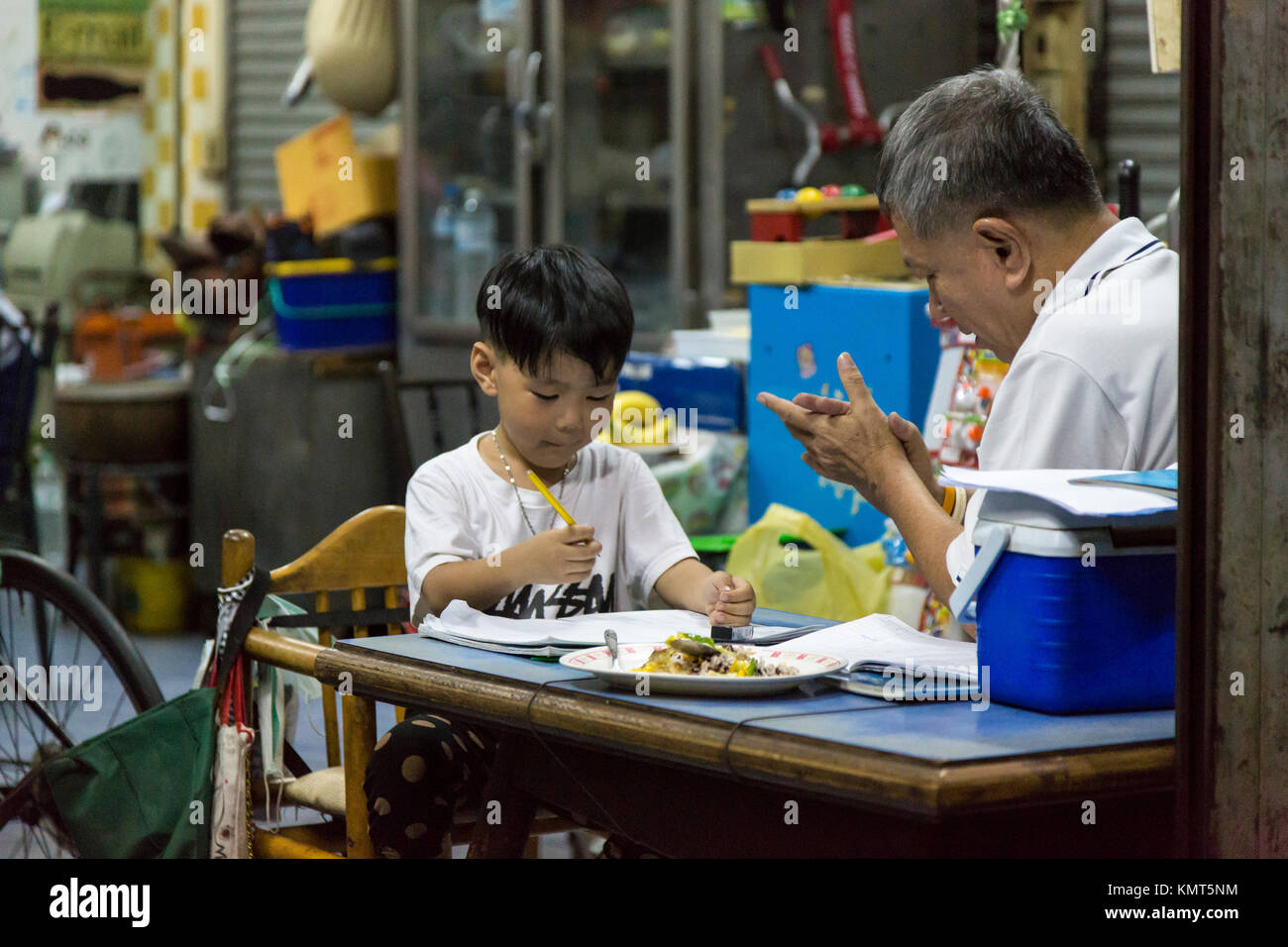 Bangkok, Thailand.  Grandfather helping Grandson with School Work at Night. Stock Photo