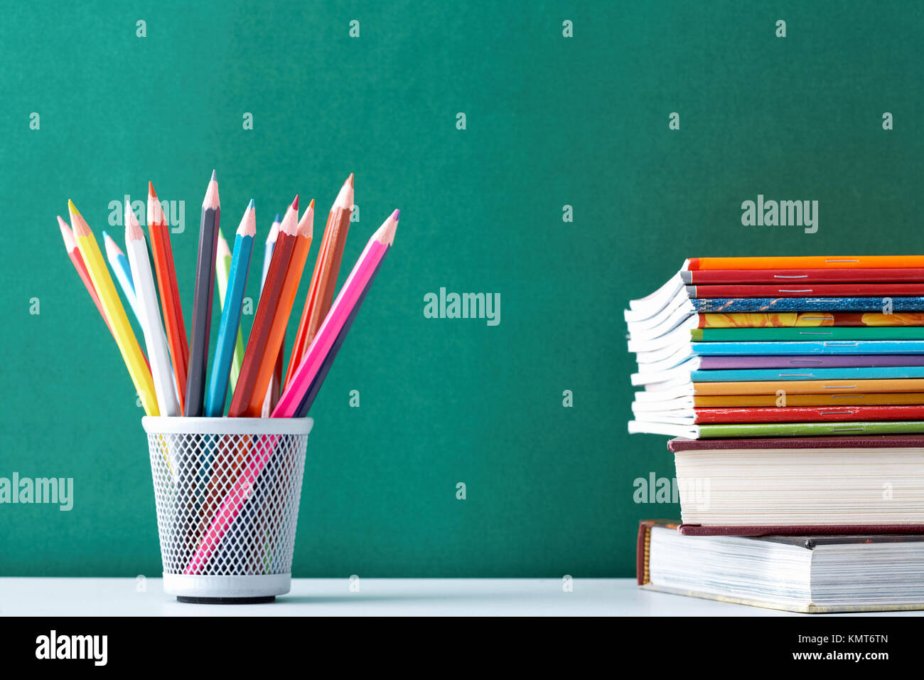 Image of crayons and exercise books against blackboard Stock Photo