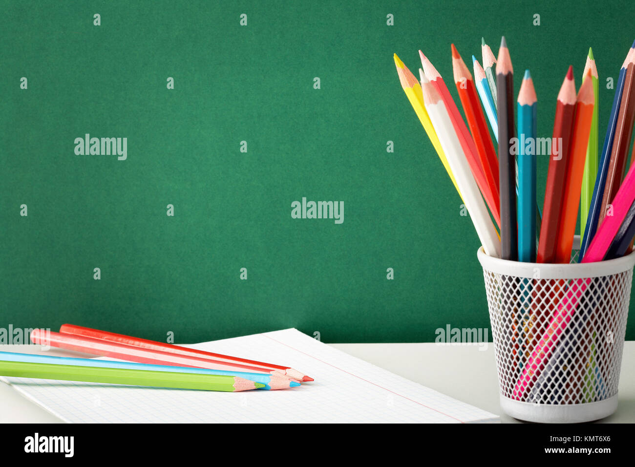 Stack of colorful pencils and open copybook near by on background of blackboard Stock Photo