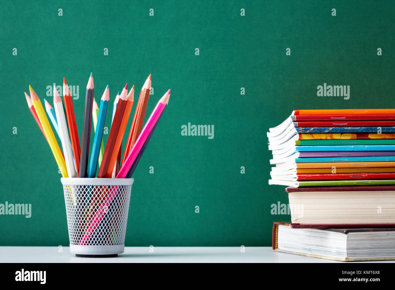 Stack of colorful textbooks and copybooks with pencils near by on background of blackboard Stock Photo