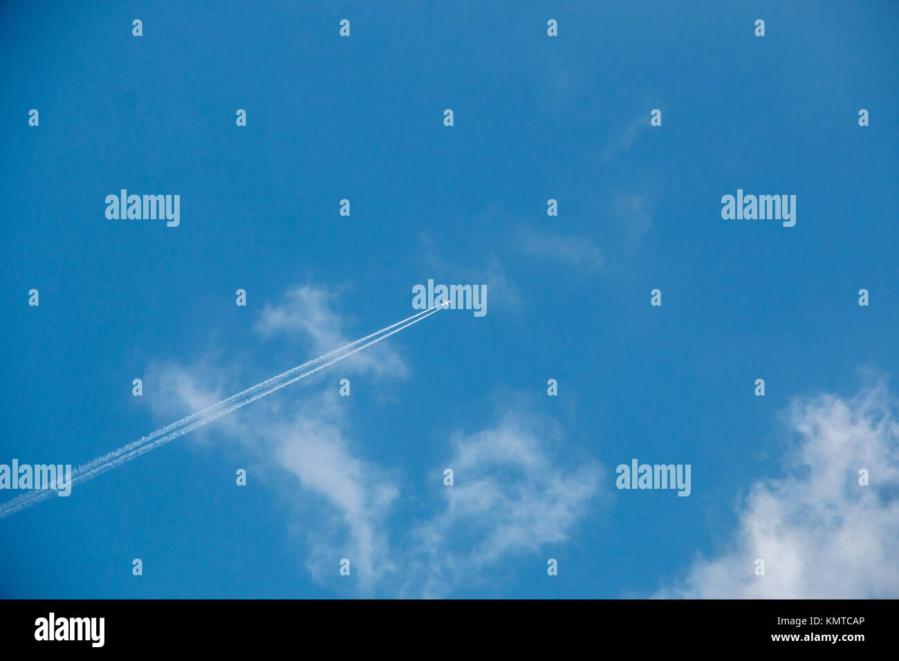 A plane far away in the sky with contrails and clouds Stock Photo