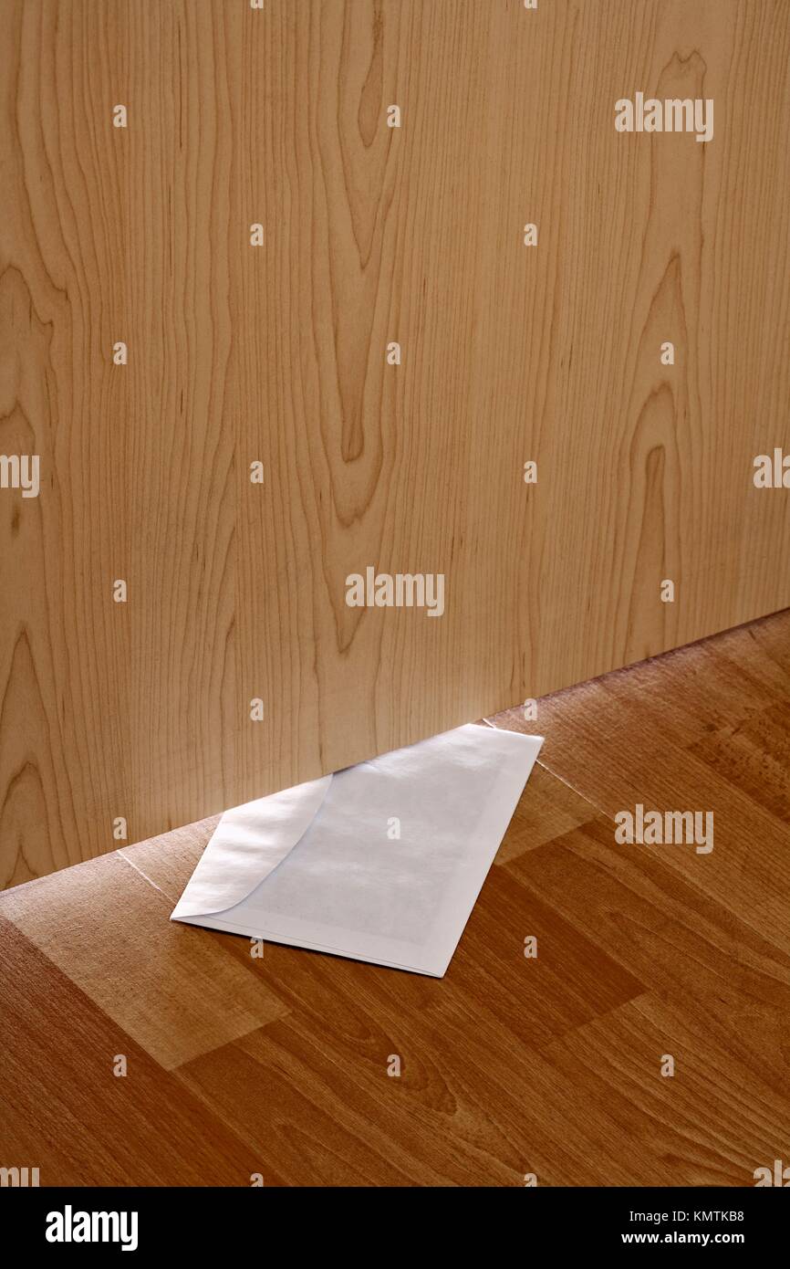White Envelope With Message Slipped Under Wooden Door Stock