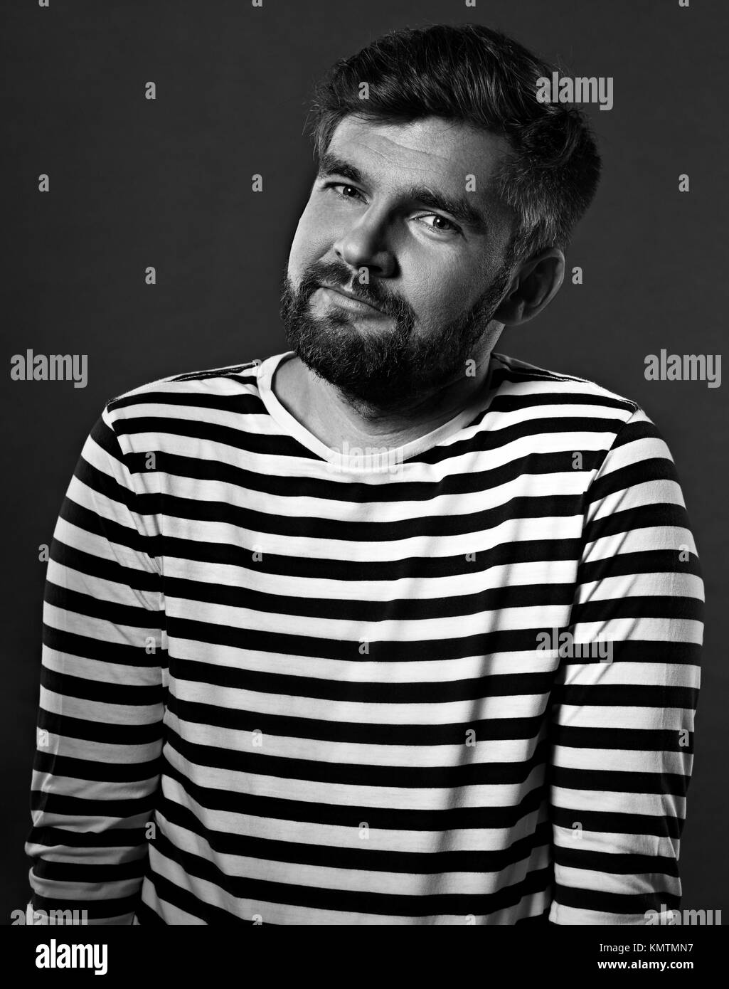 Bearded smiling emotional man in casual striped t-shirt on grey background. Closeup portrait. Black and white Stock Photo