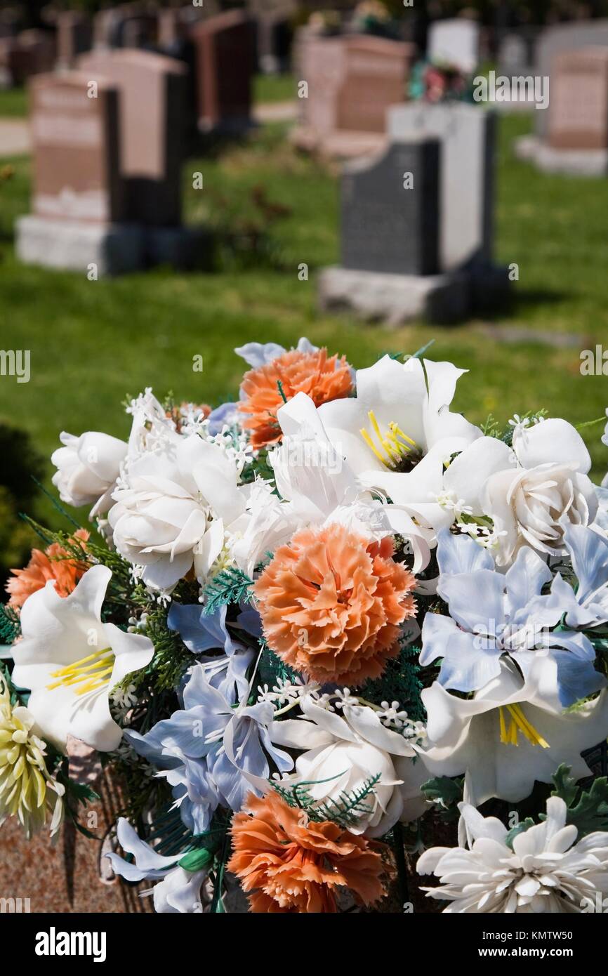 Closeup of a bouquet of artificial flowers atop a headstone in a